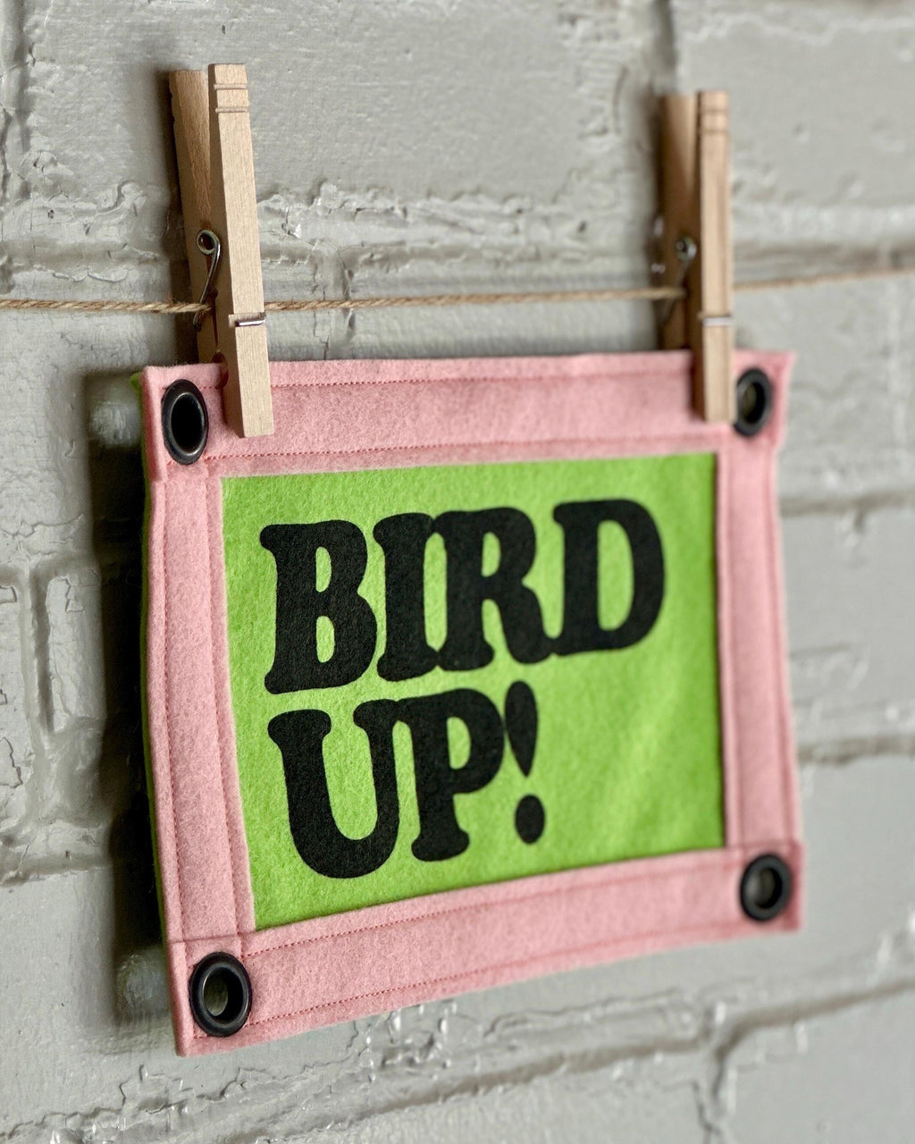 Side view of a bright green felt banner with light pink trim, and black lettering that reads "Bird up!"