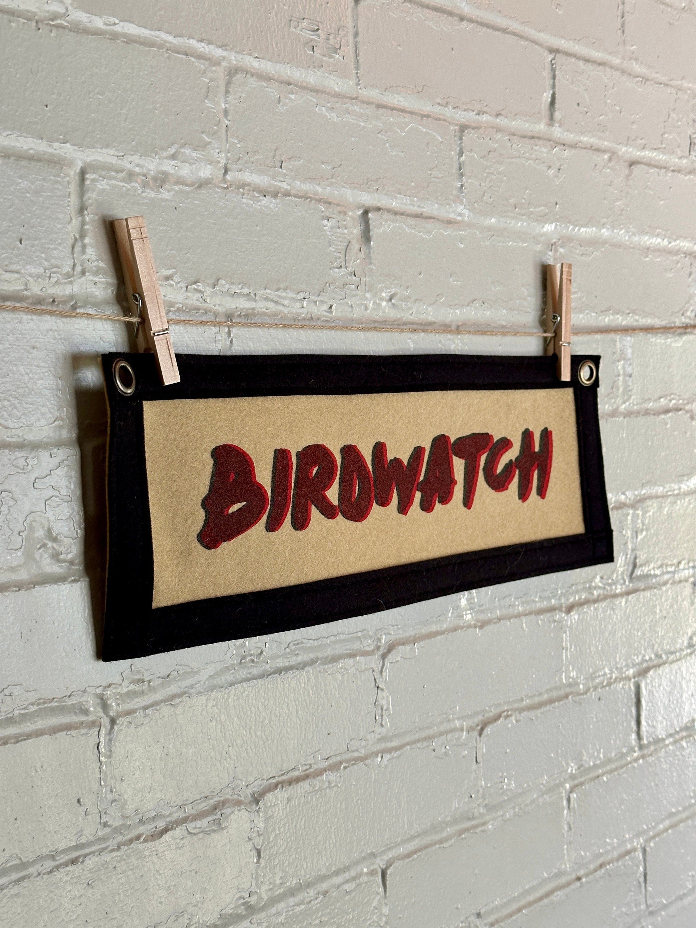 Side view of a light brown banner with black trim and double printed red and black lettering reading "BIRDWATCH"