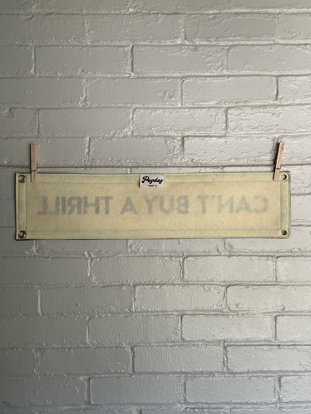 A cream felt banner with green trim and black lettering that reads "Can't Buy a Thrill"