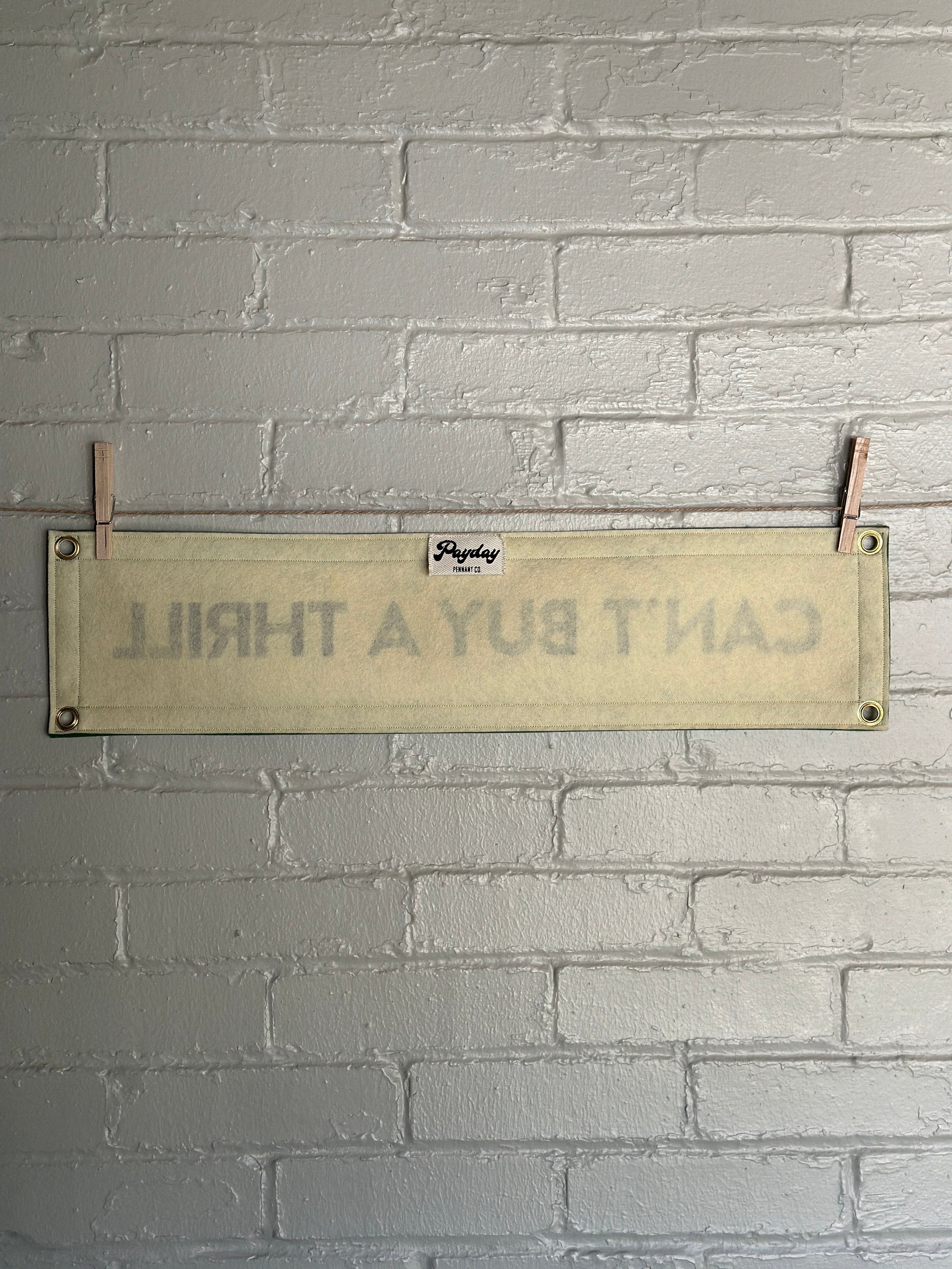 A cream felt banner with green trim and black lettering that reads "Can't Buy a Thrill"