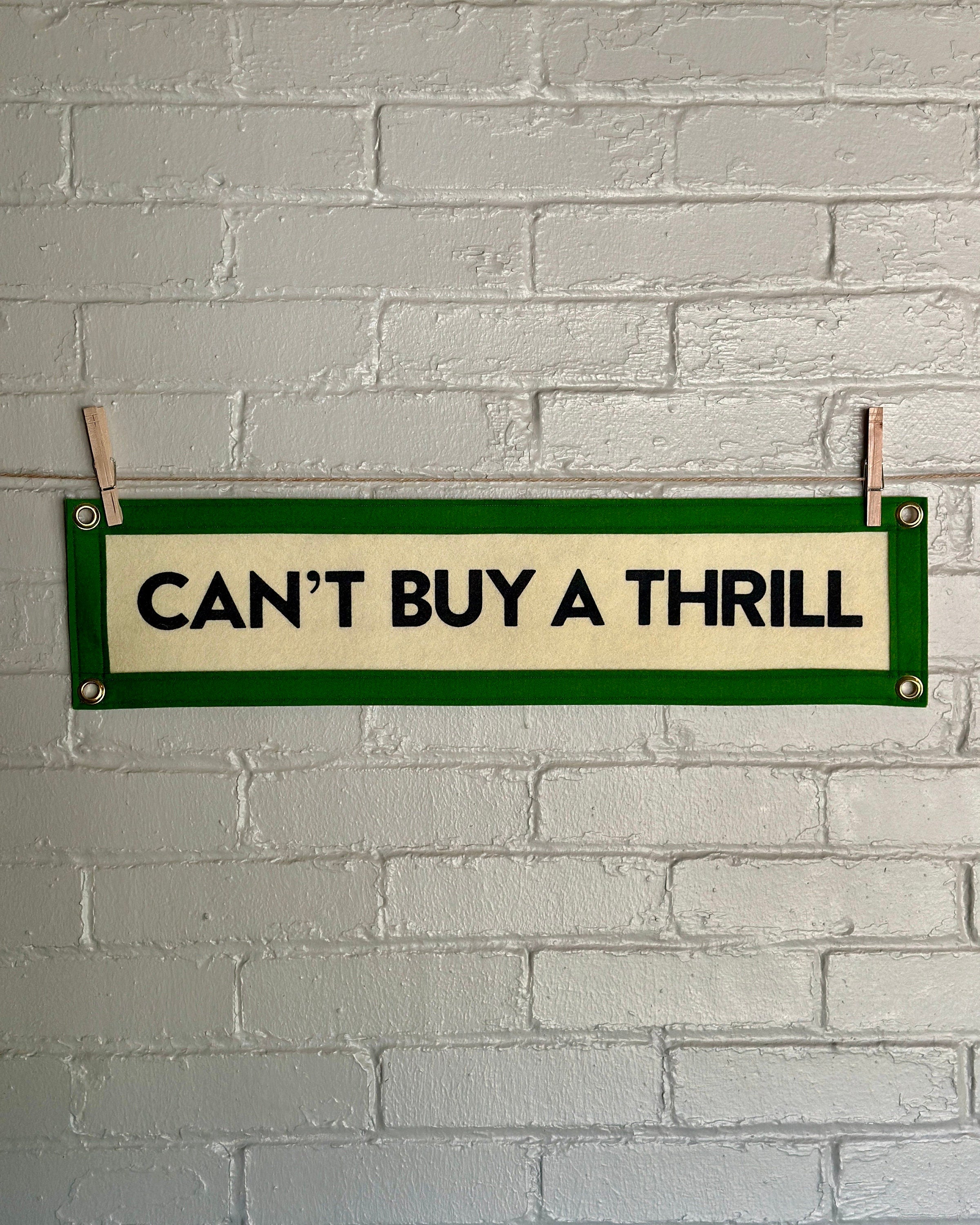 A cream felt banner with green trim and black lettering that reads "Can't Buy a Thrill"