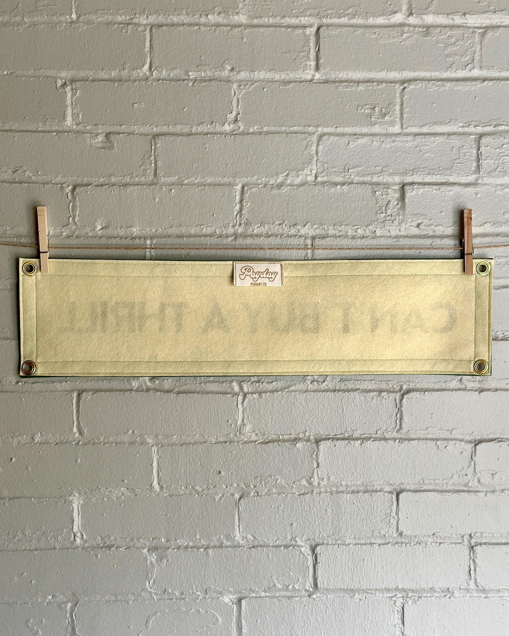 Back of a cream felt banner with green trim and gold lettering that reads "Can't Buy a Thrill"