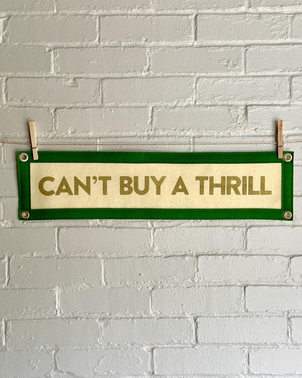 A cream felt banner with green trim and gold lettering that reads "Can't Buy a Thrill"
