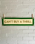 A cream felt banner with green trim and gold lettering that reads "Can't Buy a Thrill"