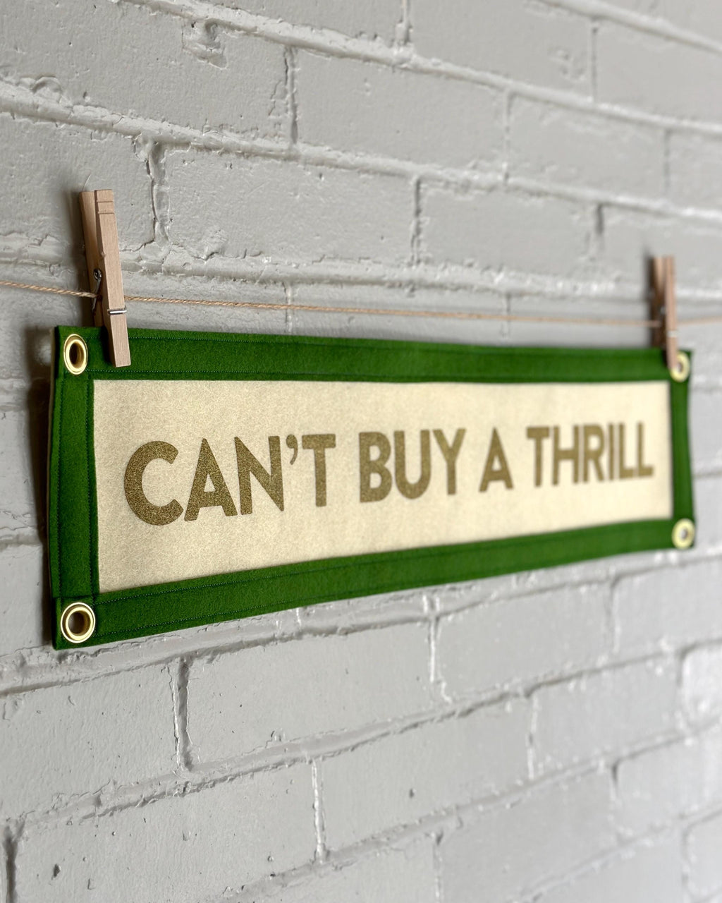 Side of a cream felt banner with green trim and gold lettering that reads "Can't Buy a Thrill"