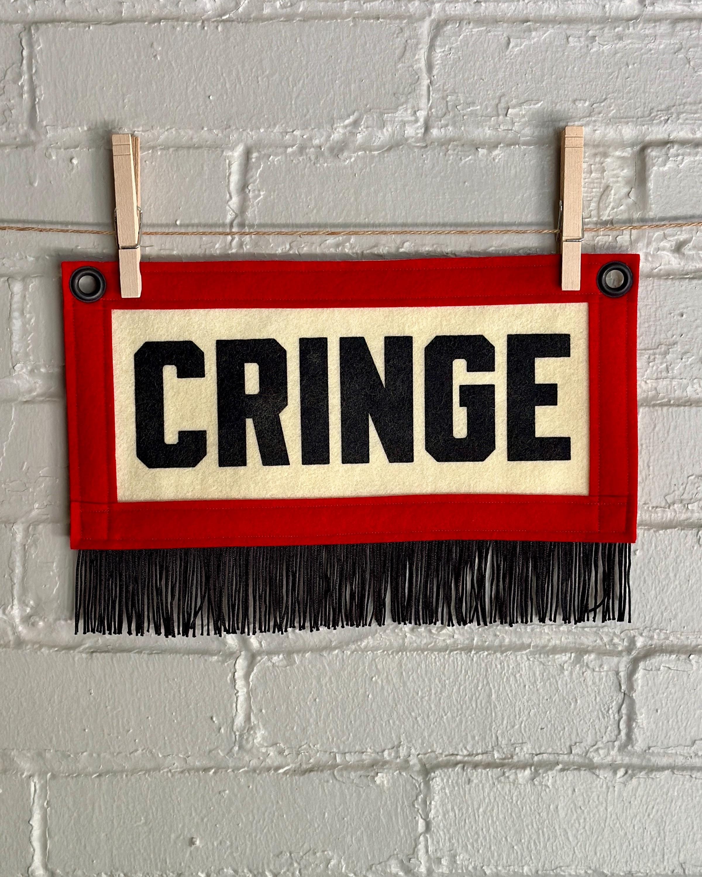 A cream felt banner with red trim, black fringe, and black lettering that reads 'CRINGE'