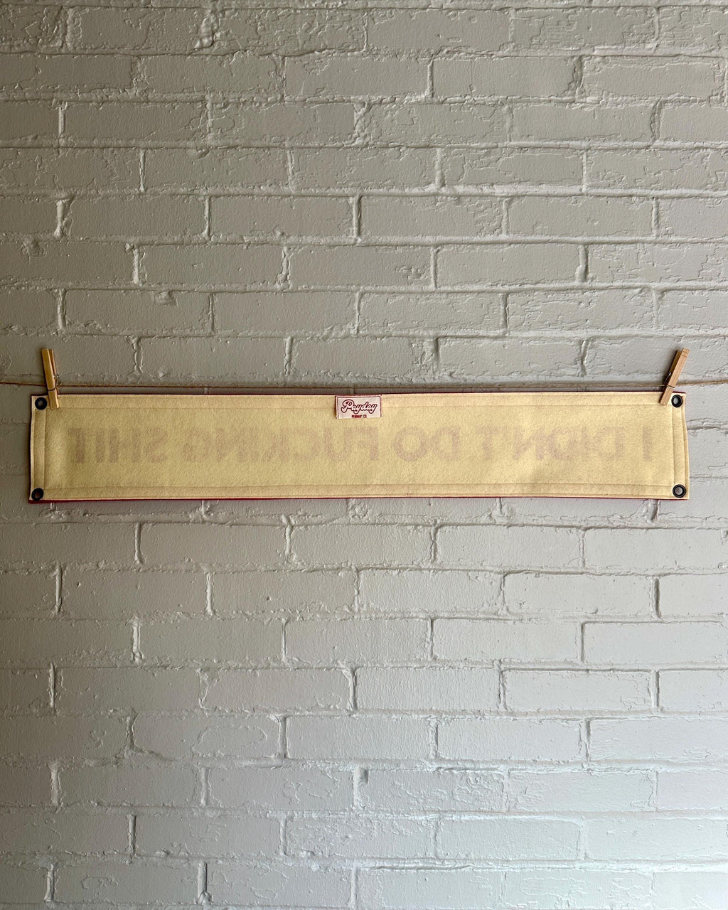 Back of a cream felt banner with red trim and lettering that reads "I didn't do fucking shit"