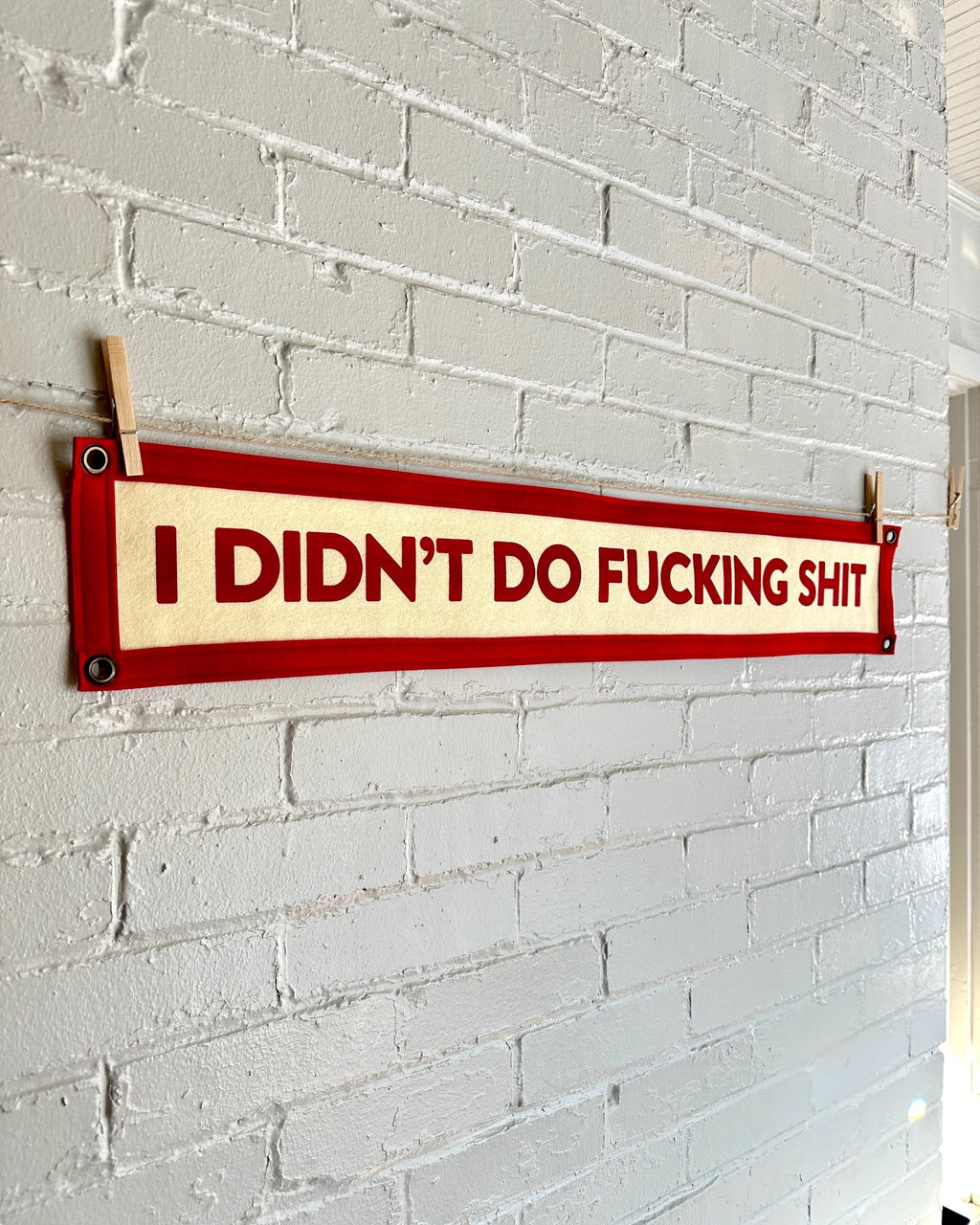 Side view of a cream felt banner with red trim and lettering that reads "I didn't do fucking shit"