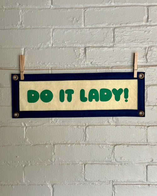 A cream felt banner with navy trim and green lettering that reads "Do it lady!"