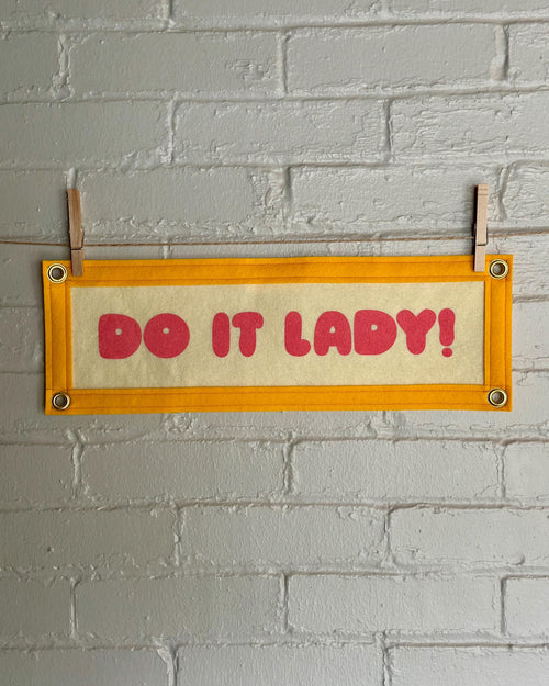 A cream felt banner with yellow trim and pink lettering that reads "Do it lady!"