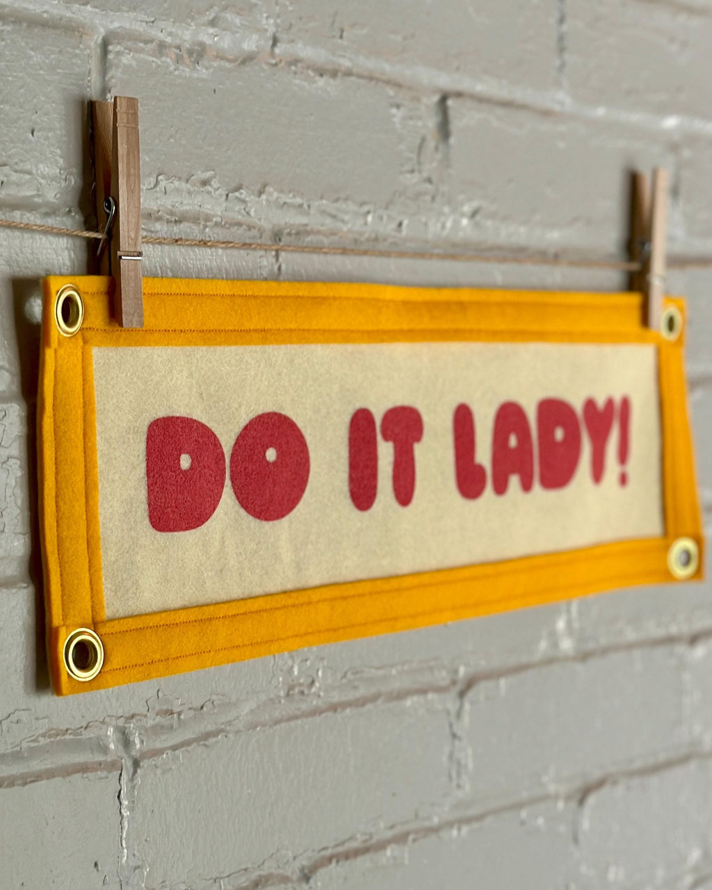 Side view of a cream felt banner with yellow trim and pink lettering that reads "Do it lady!"