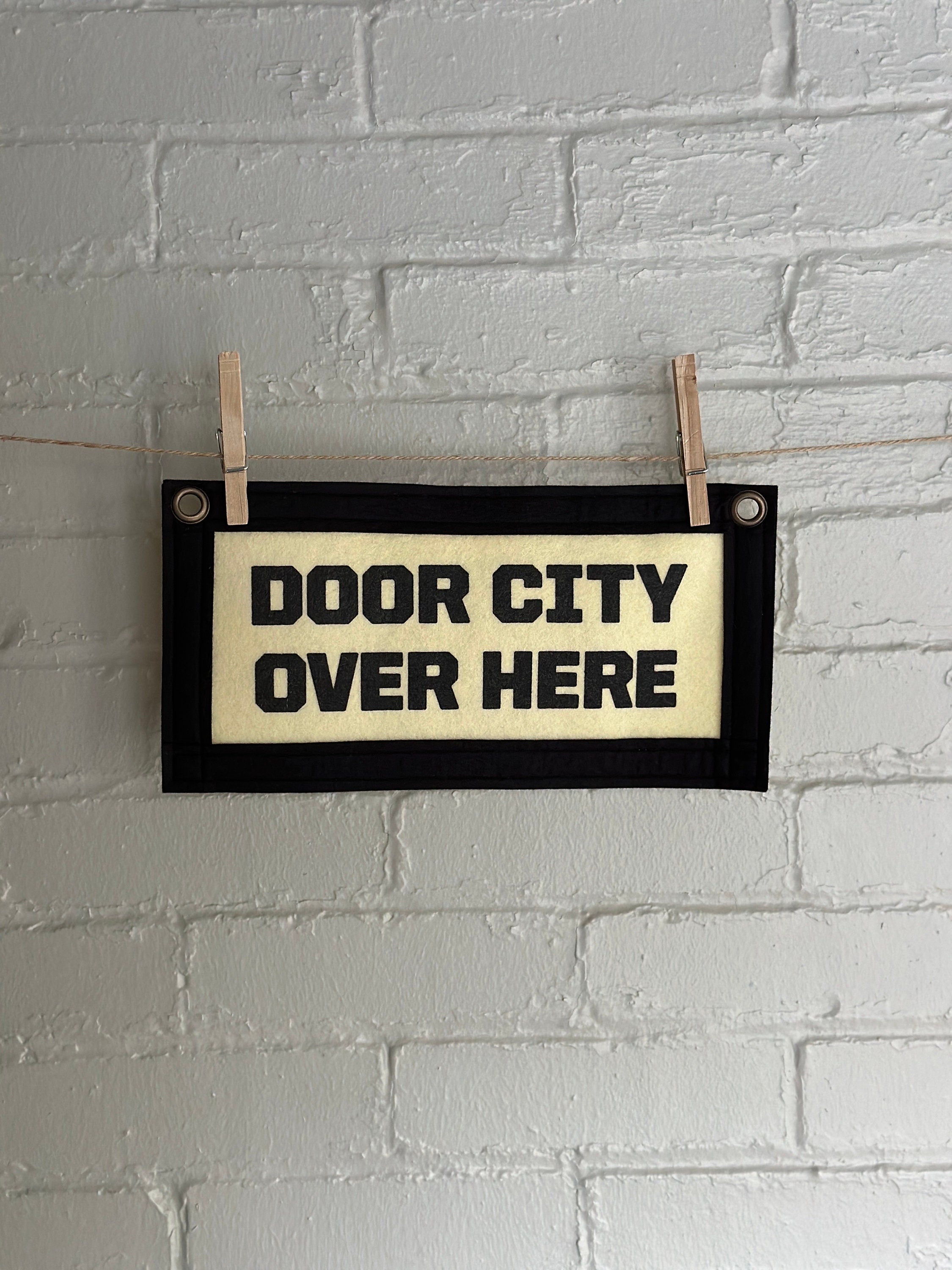 Cream banner with black felt trim and lettering that reads "door city over here"