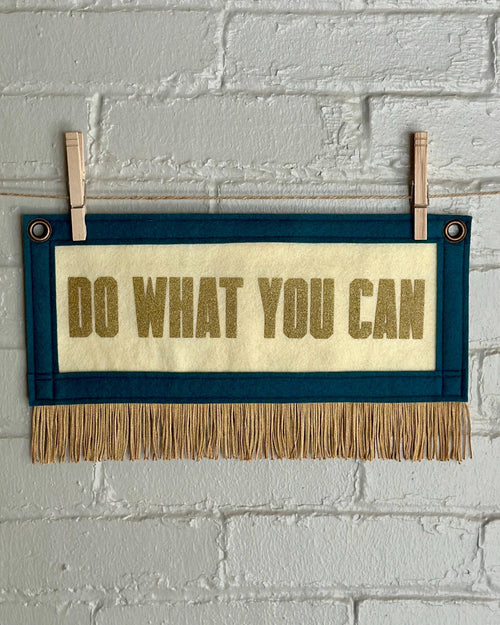 A cream felt banner with blue spruce trim, gold fringe and lettering that reads "Do what you can"