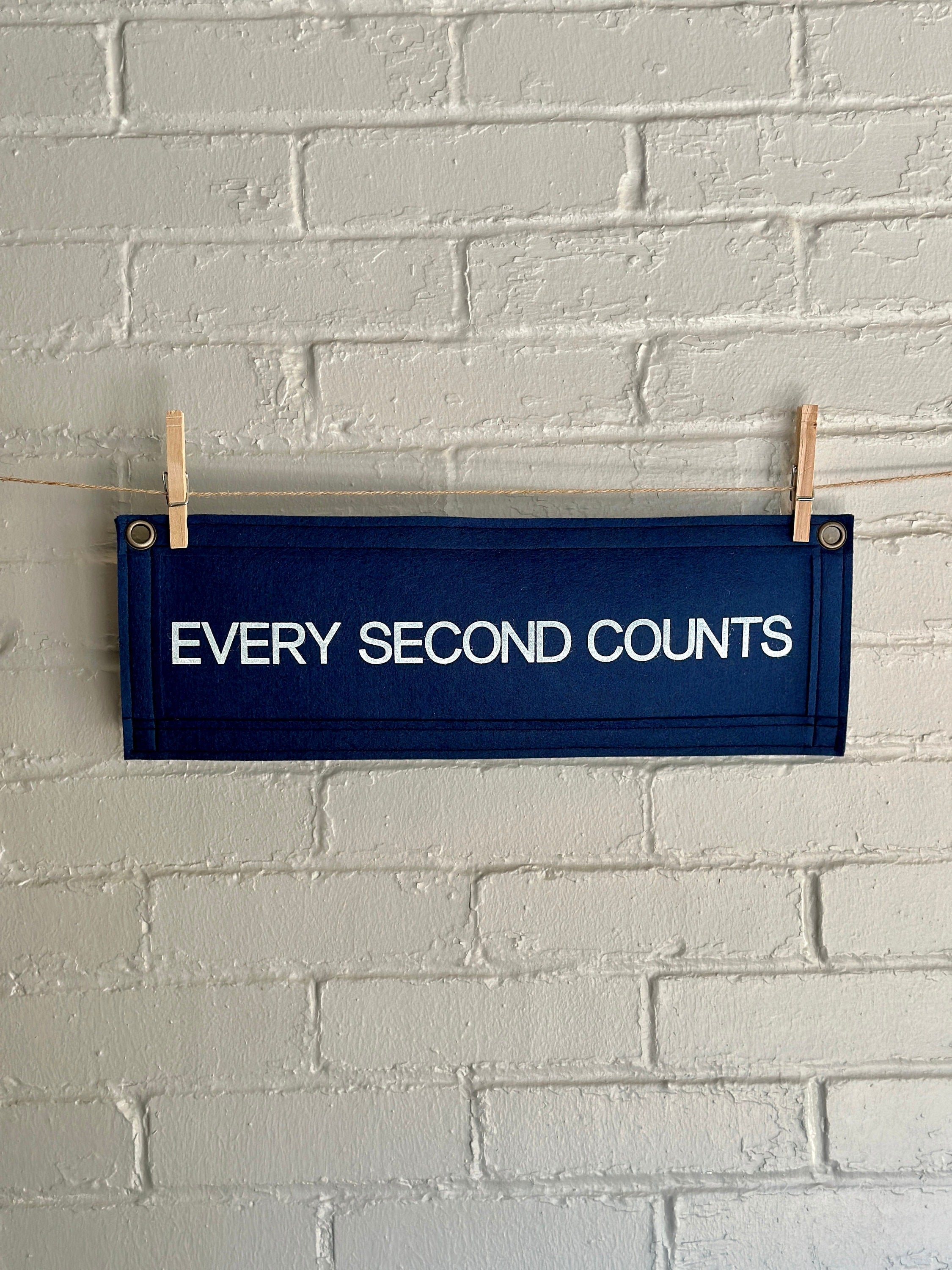 A navy felt banner with navy trim and bright white lettering which reads "every second counts"