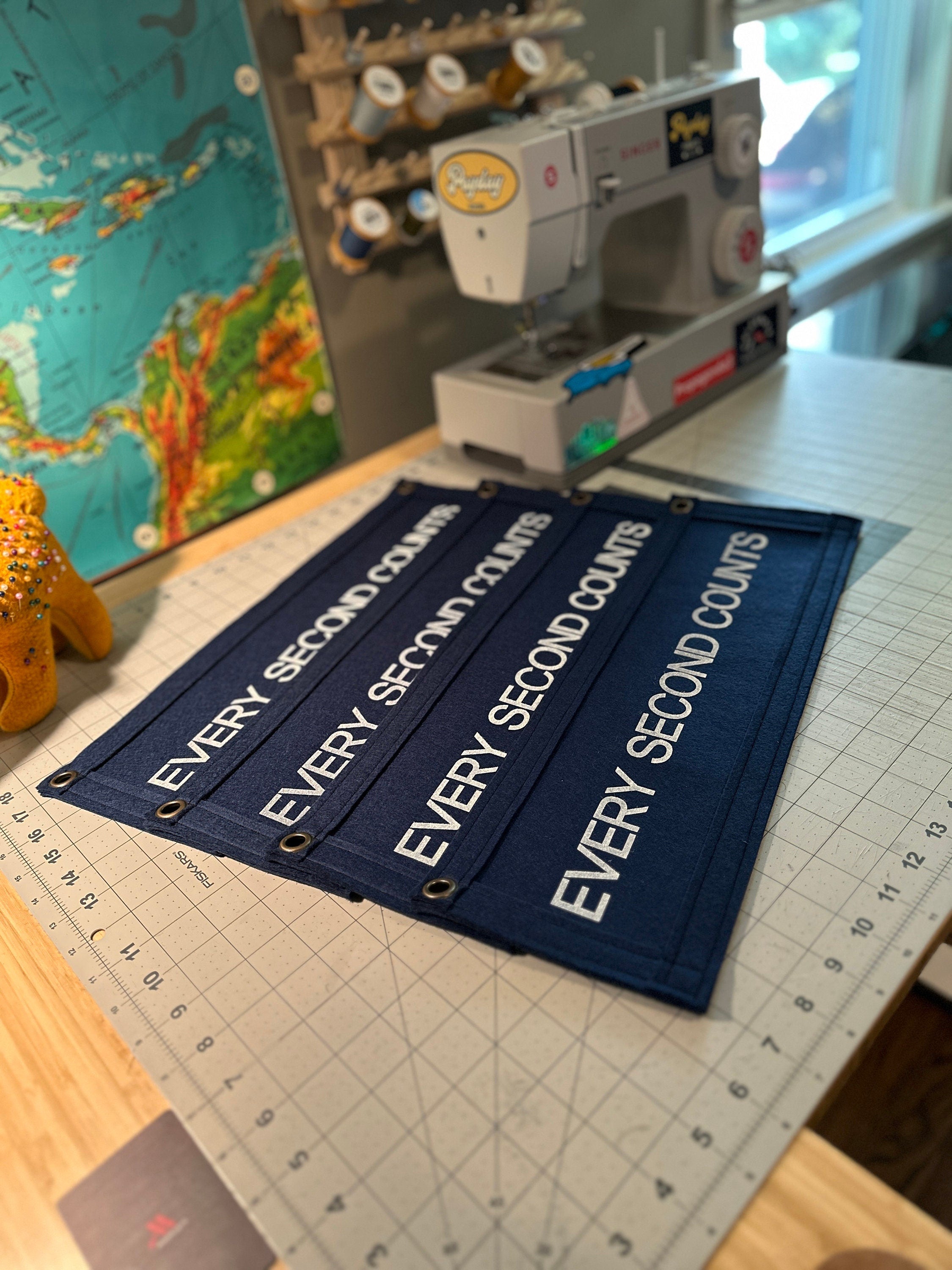 Four navy banners on a cutting table beside a sewing machine