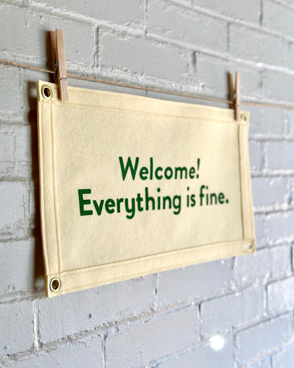 Side view of a cream felt banner with green lettering referencing The Good Place reading "Welcome! Everything is fine."