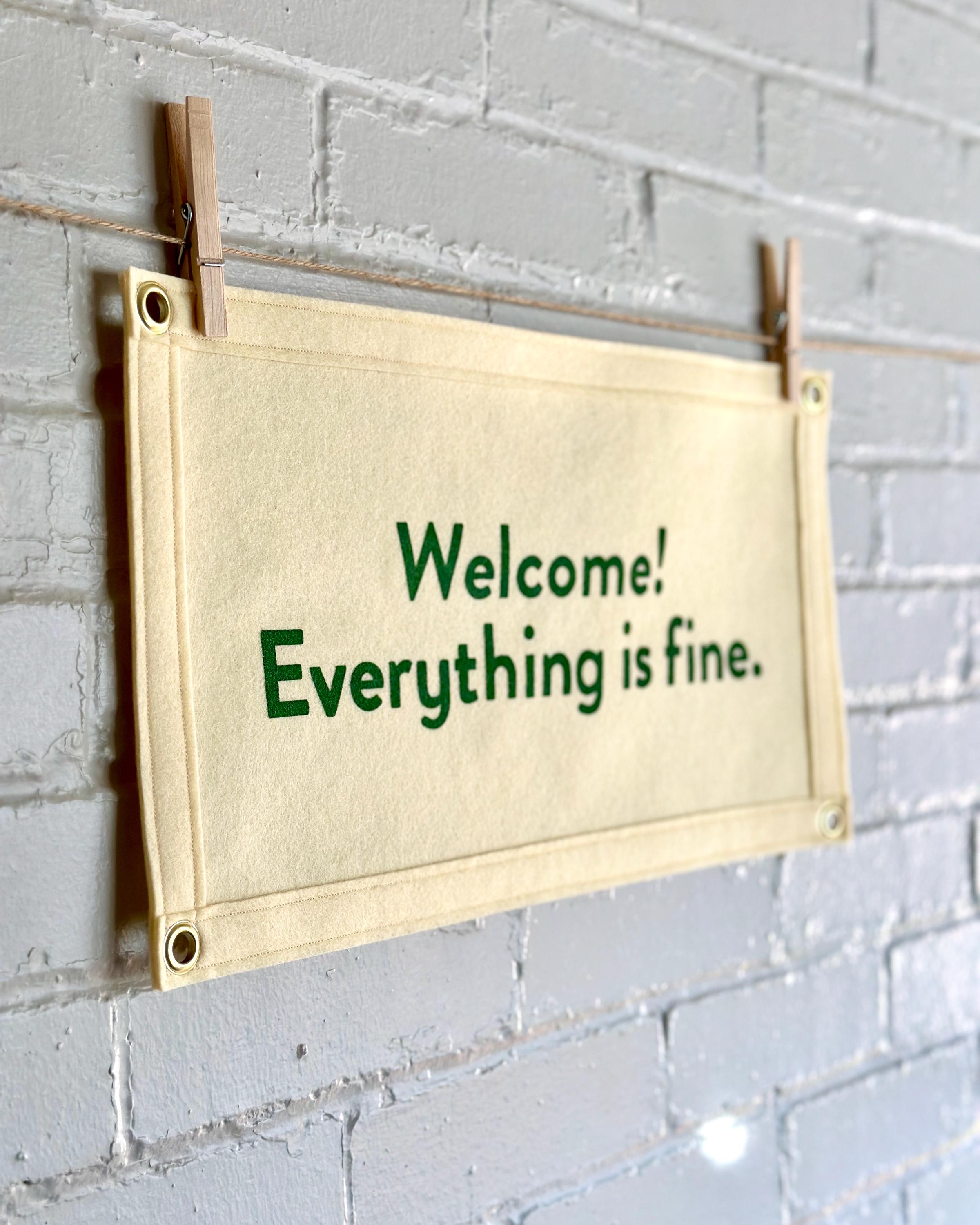 Side view of a cream felt banner with green lettering referencing The Good Place reading "Welcome! Everything is fine."