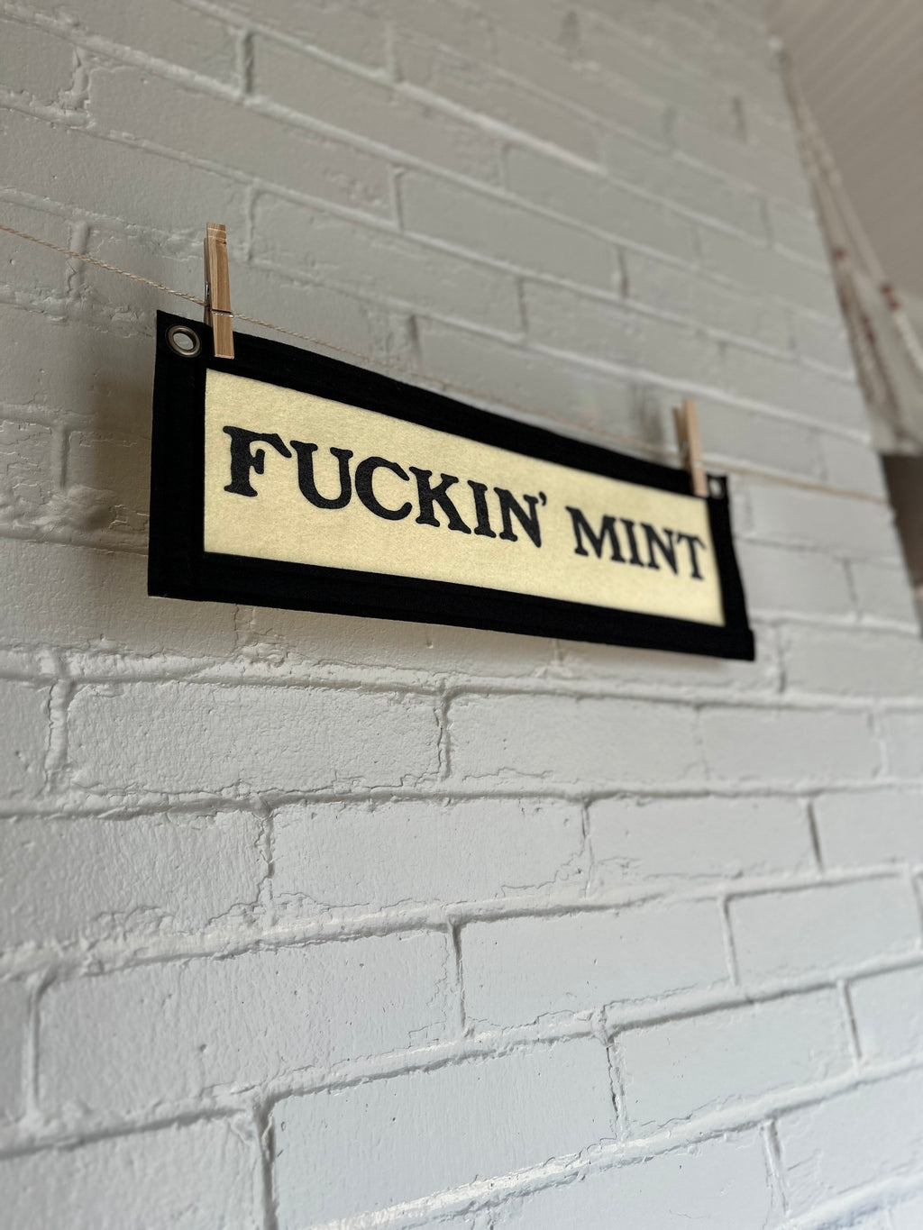 Side view of a cream felt banner with black trim and lettering that reads "fuckin' mint"