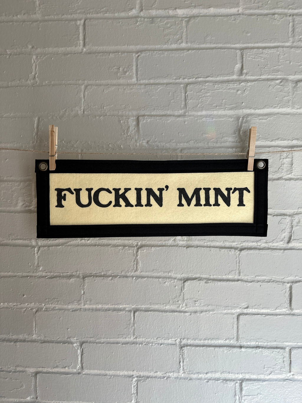A cream felt banner with black trim and lettering that reads "fuckin' mint"