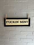 A cream felt banner with black trim and lettering that reads "fuckin' mint"