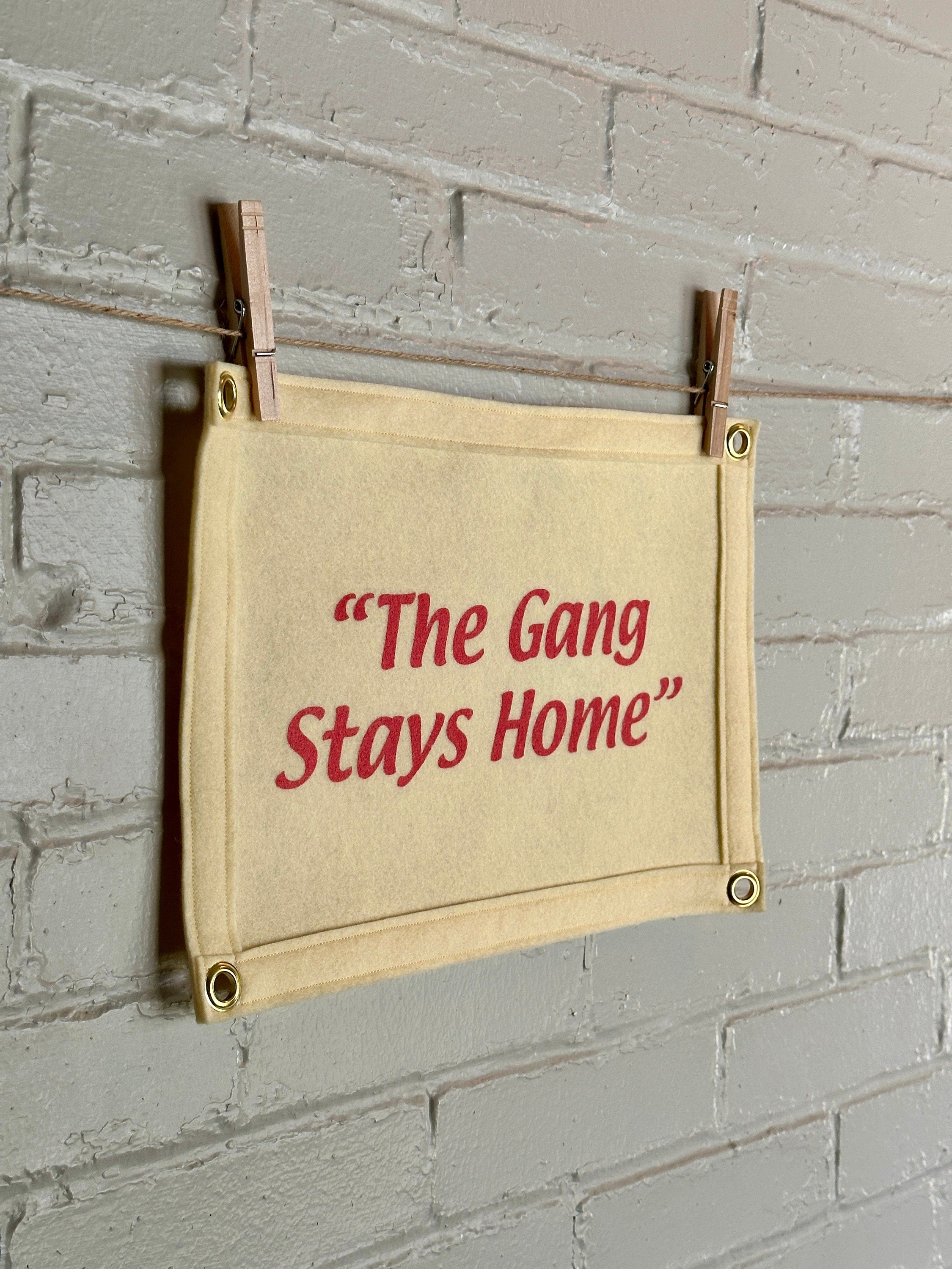 Side view of a cream banner with cream felt trim and pink lettering that reads "the gang stays home"