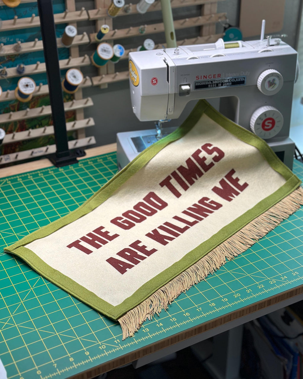 A partially completed Good Times felt banner on a desk with a sewing machine