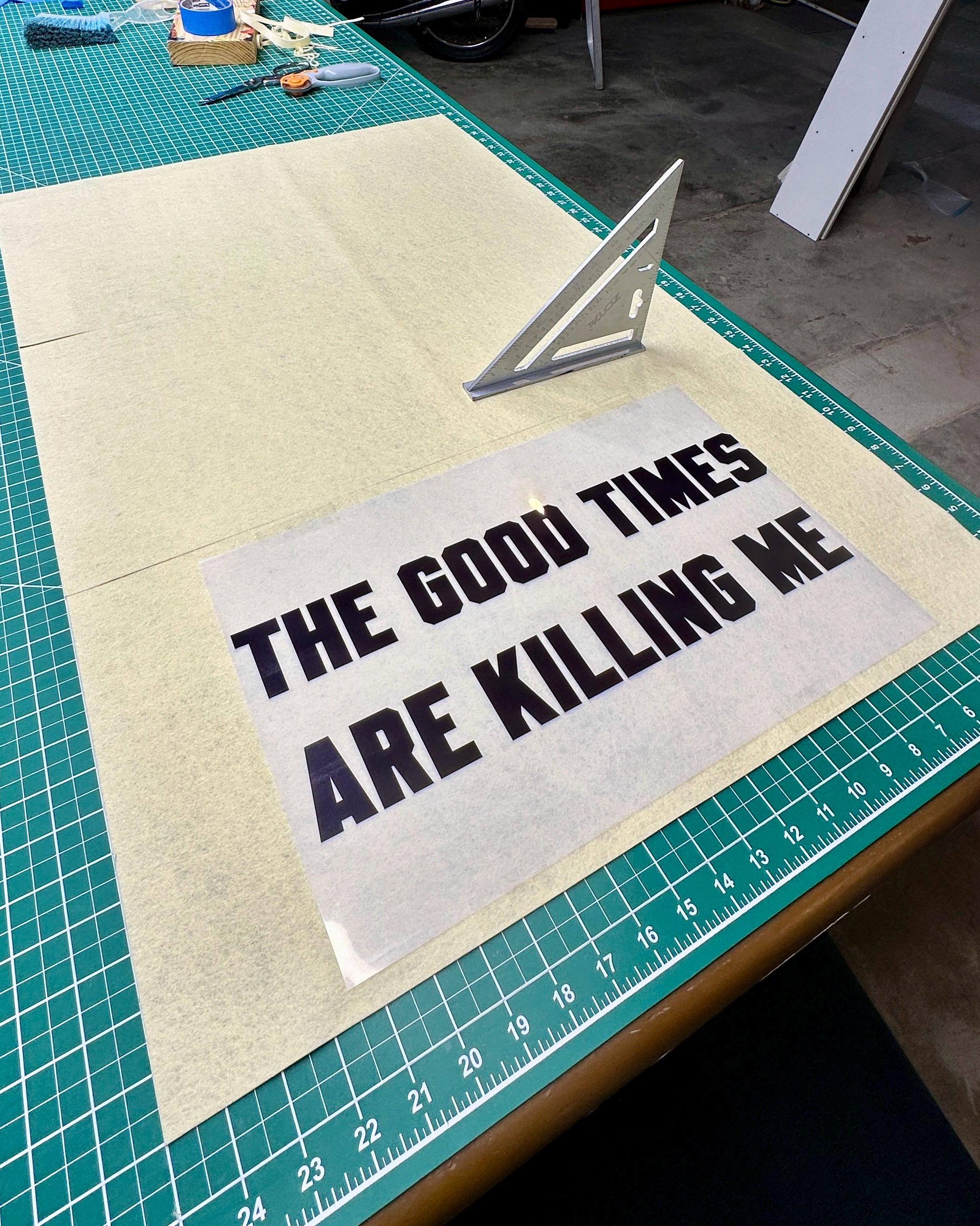 Three slices of cream felt on a large cutting table with a carpenter square and a transparency sheet with "the good times are killing me" printed on