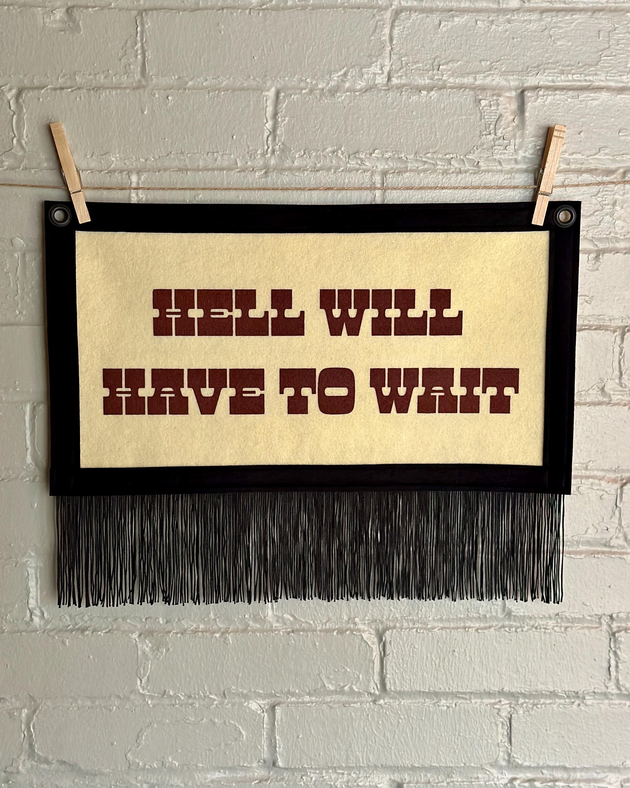 Cream felt banner with black trim, long black fringe, and blood red lettering reading "Hell will have to wait"