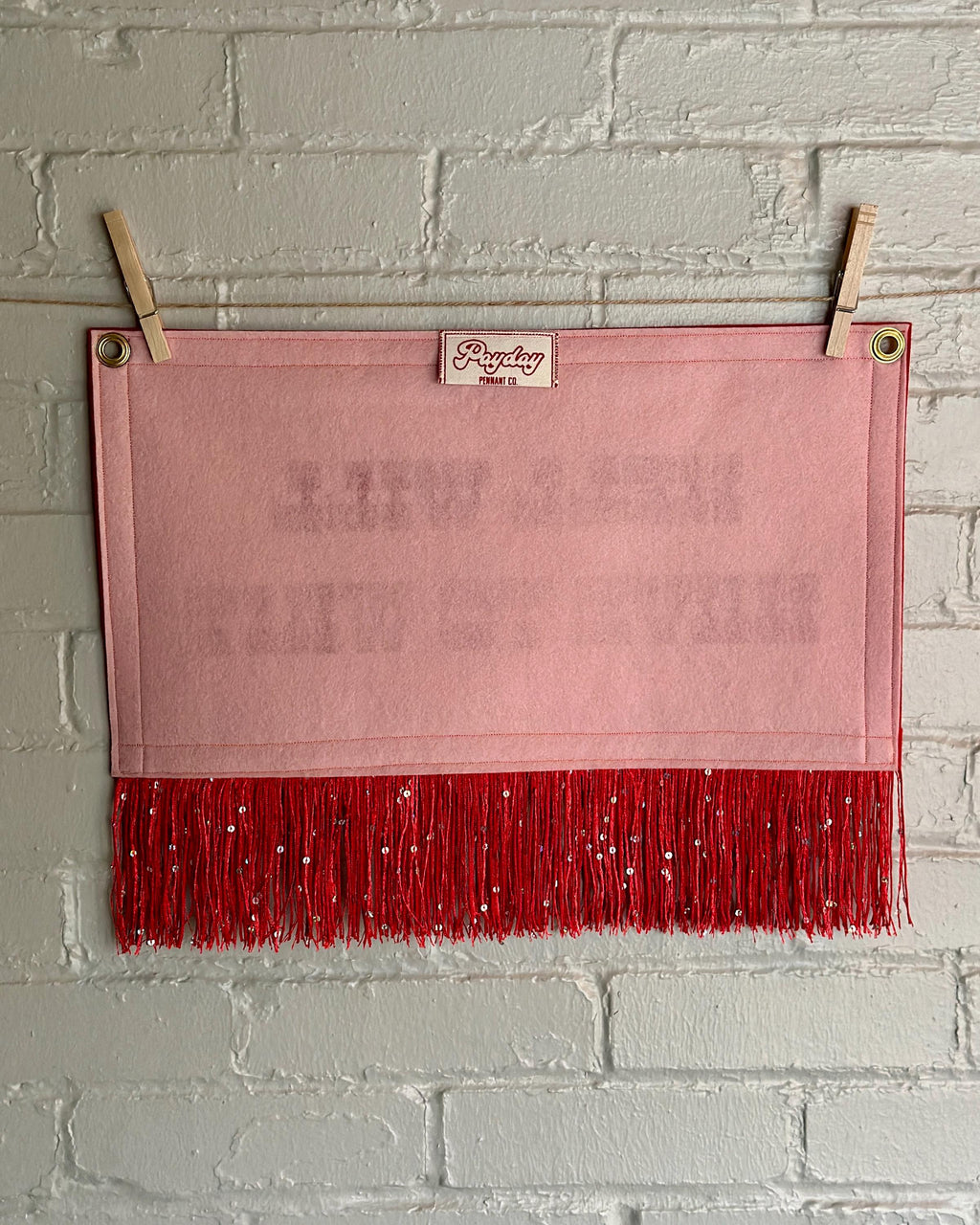 Back of a cream felt banner with red trim, long red sequin fringe, and red lettering reading "Hell will have to wait"