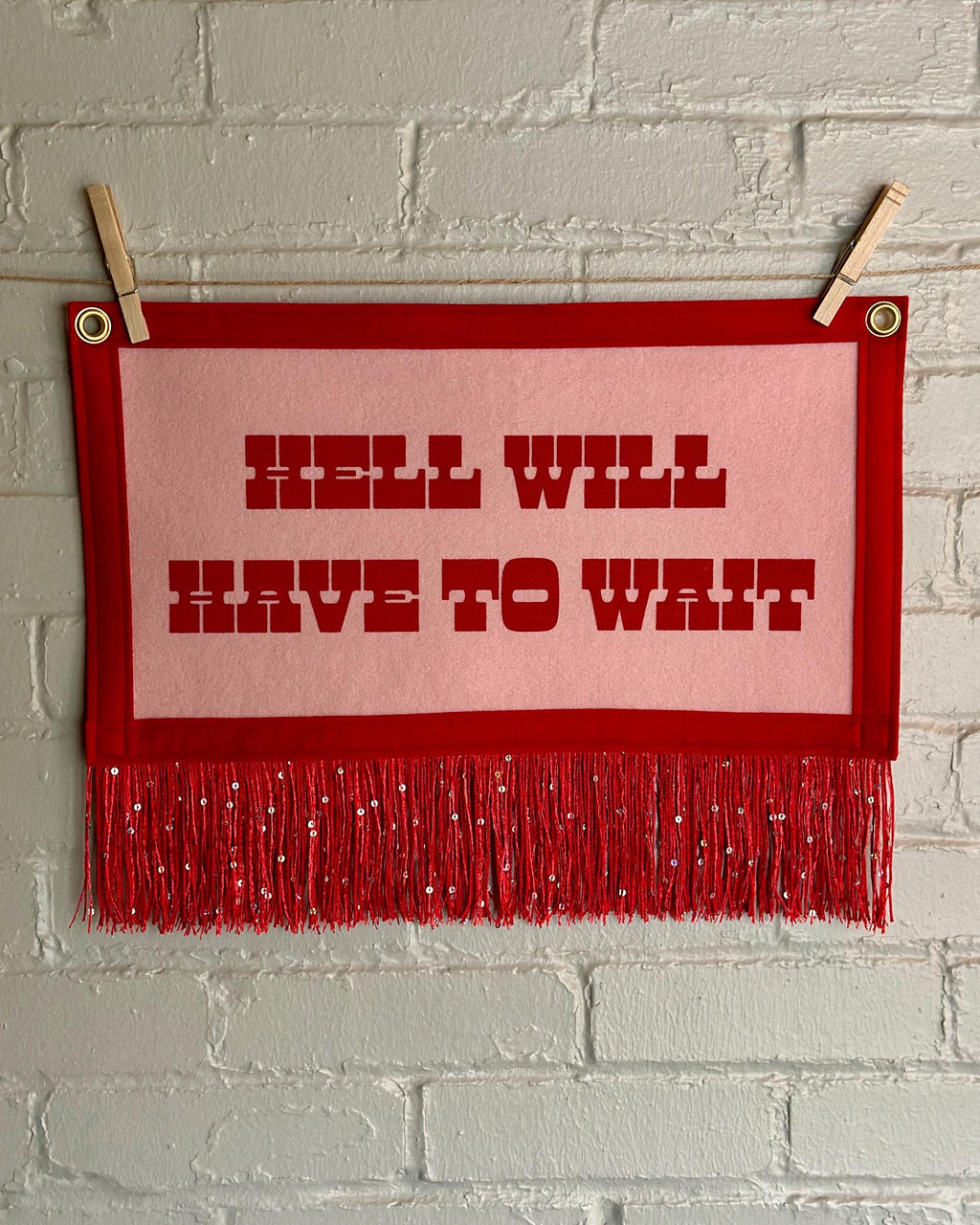 Cream felt banner with red trim, long red sequin fringe, and red lettering reading "Hell will have to wait"