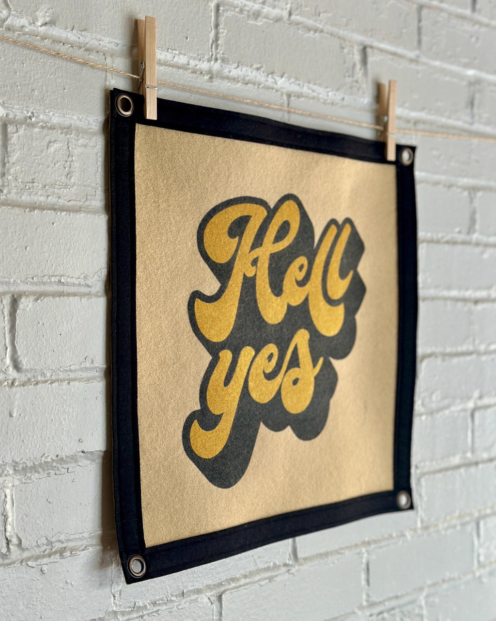 Side view of a light brown banner with black trim and a large stylized vintage lettering in black and yellow ink that reads "Hell yes"