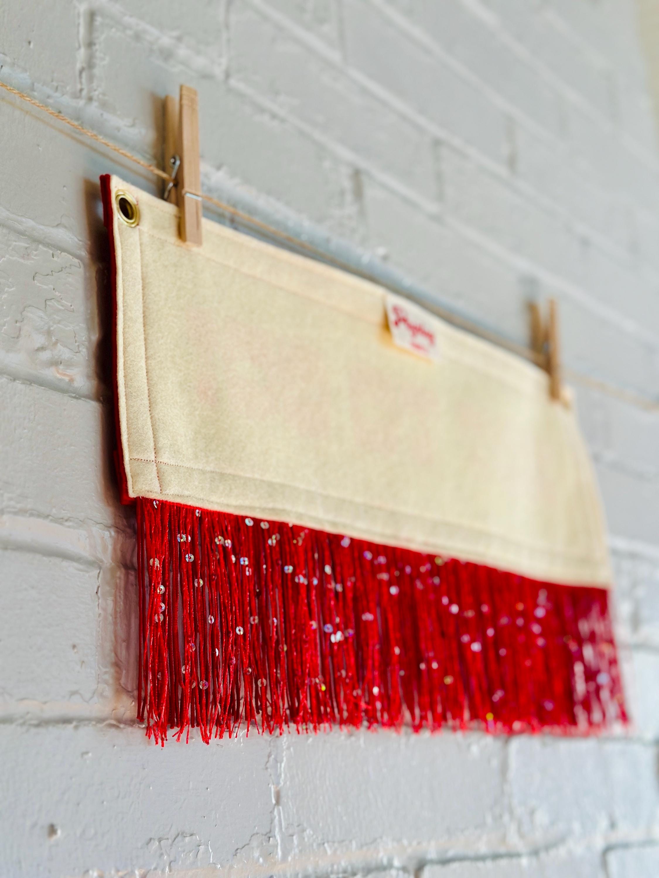 The back of a cream felt banner with red trim and red sequin fringe, pink lettering reads "HOT TO GO!"