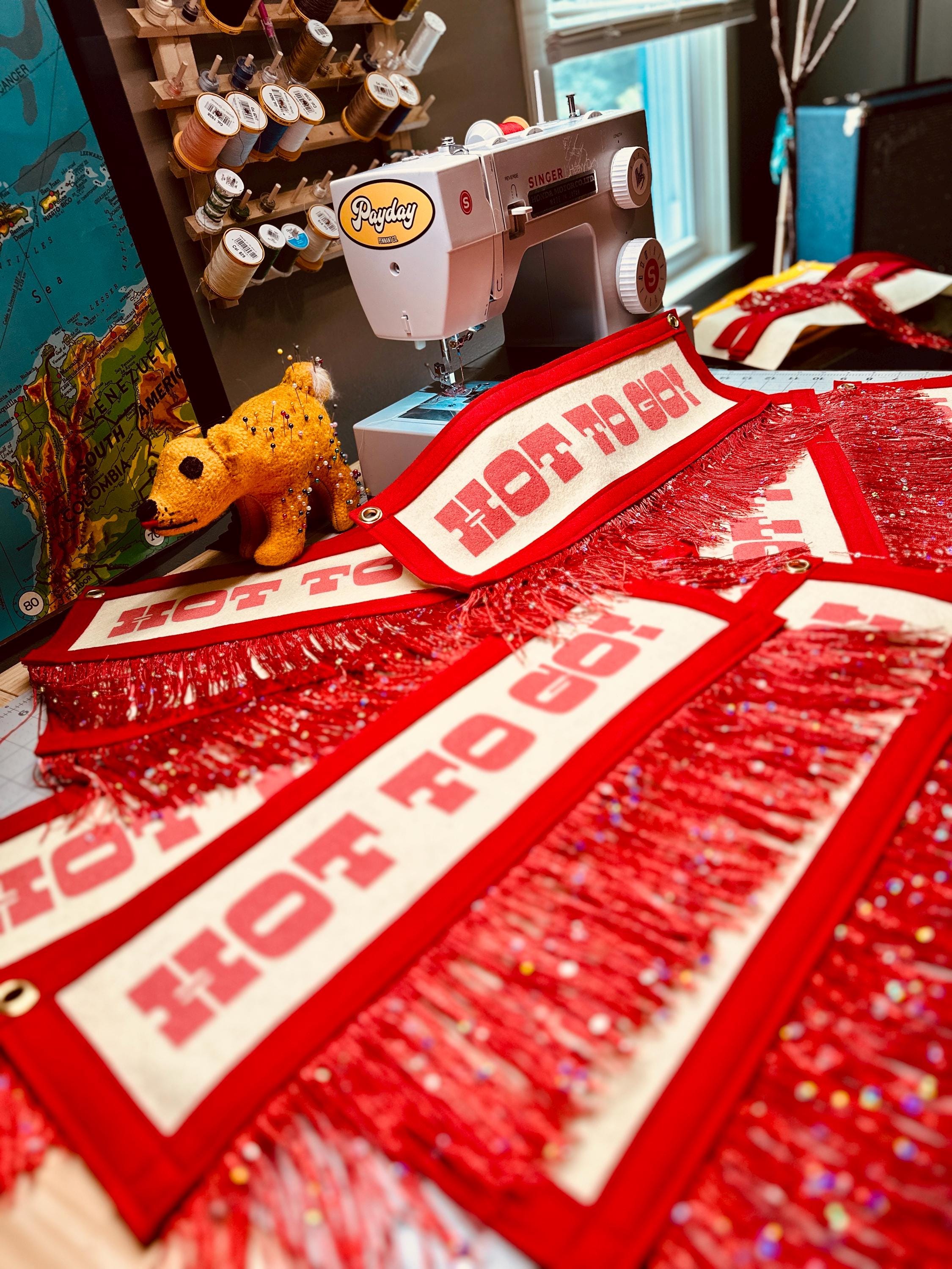 A soft-focus photo of many red fringe HOT TO GO! banners scattered across a desk and beside a sewing machine