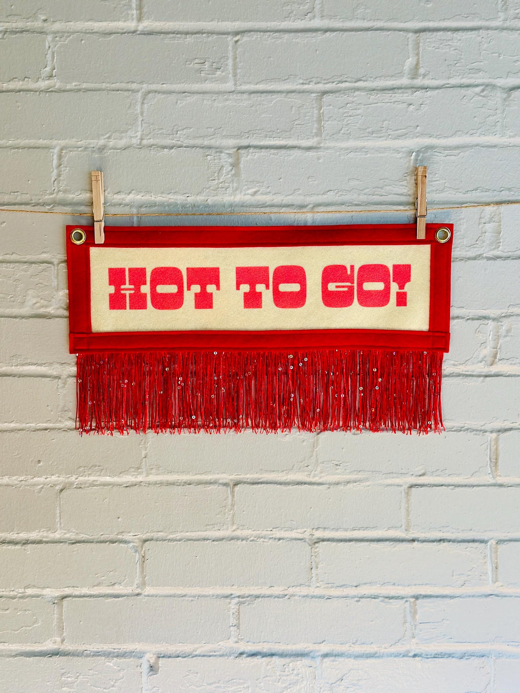 A cream felt banner with red trim and red sequin fringe, pink lettering reads "HOT TO GO!"