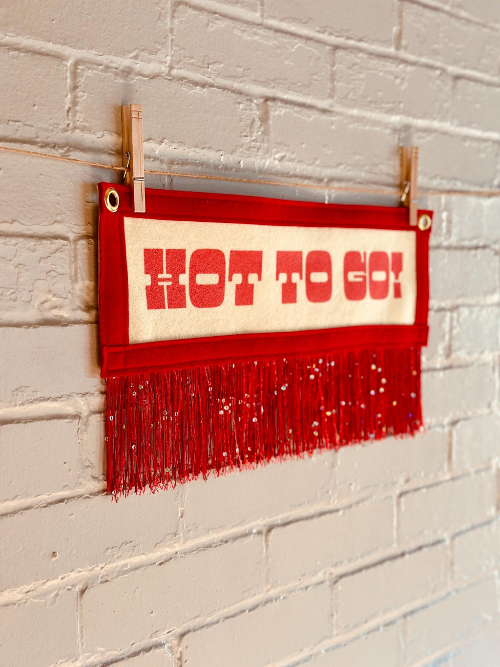 Side view of a cream felt banner with red trim and red sequin fringe, pink lettering reads "HOT TO GO!"