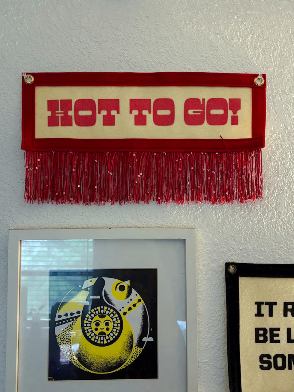 A red HOT GO GO! banner hung on a white wall alongside other framed artwork