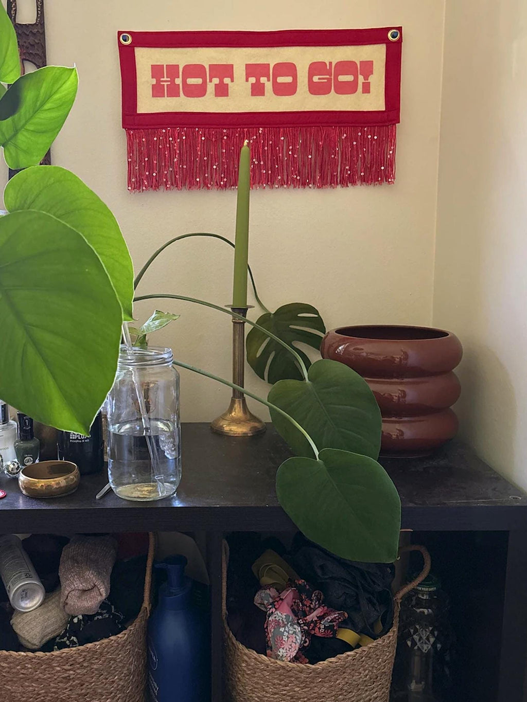 A red HOT TO GO! banner hung in a home above a desk with candle and monstera plants