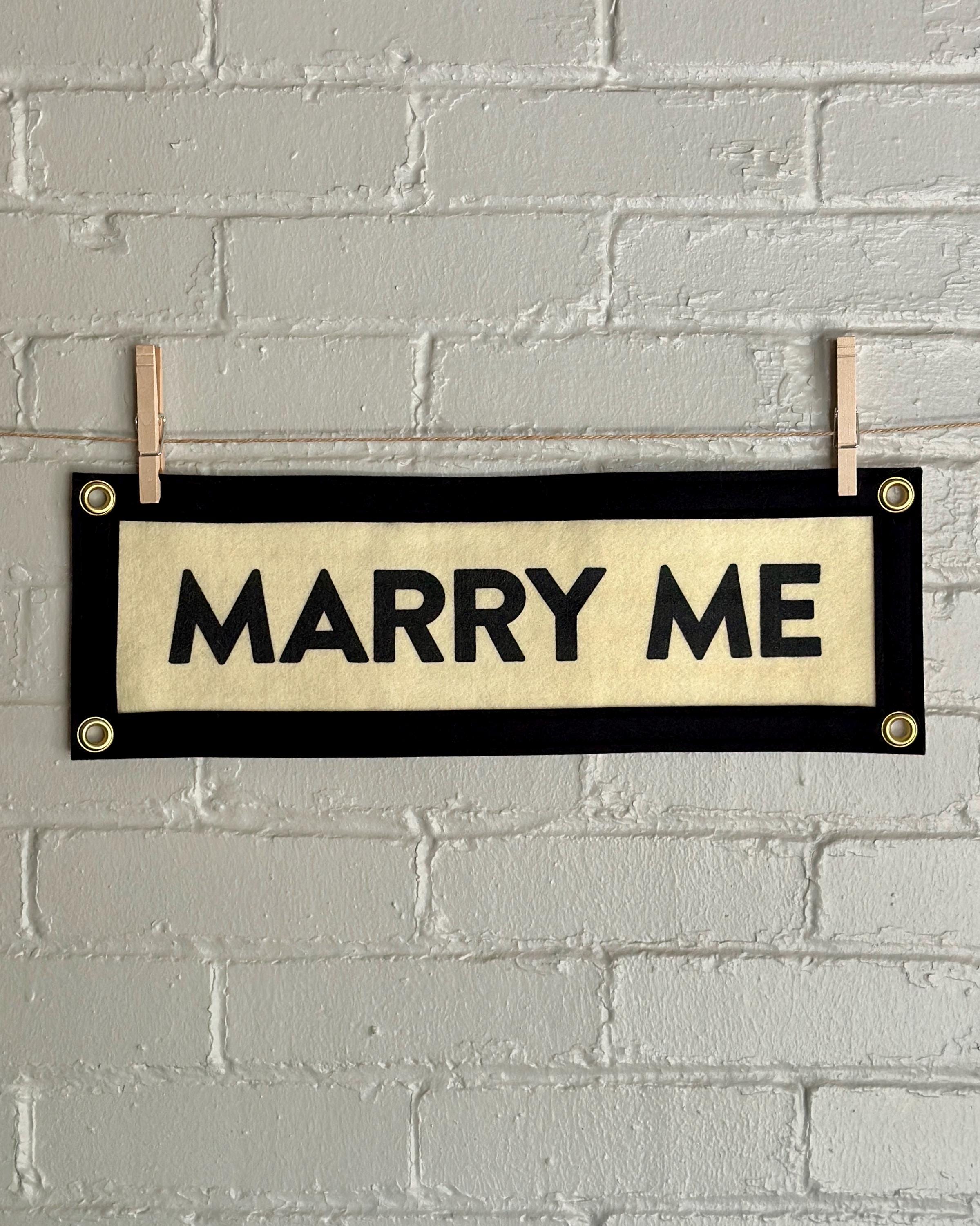 Cream felt banner with black trim and lettering reading 'MARRY ME'