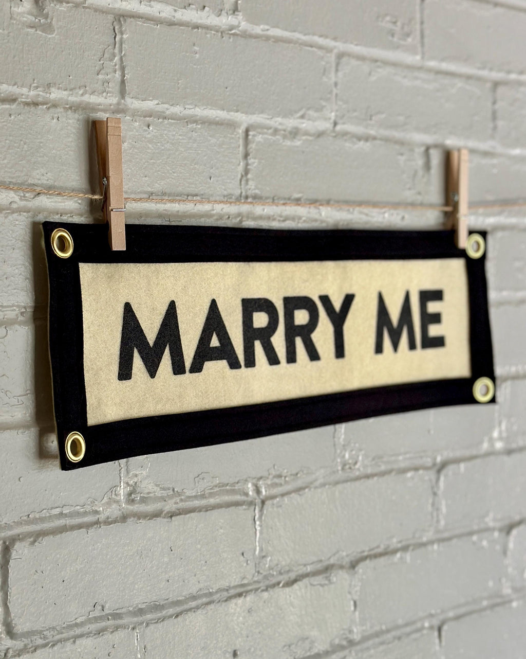Side view of a cream felt banner with black trim and lettering reading 'MARRY ME'