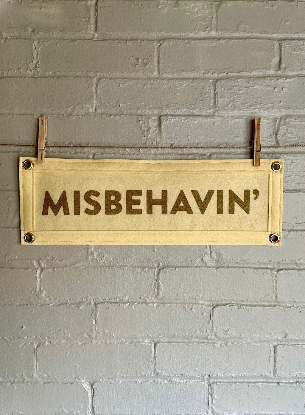 Cream felt banner with cream trim and gold ink lettering that reads "MISBEHAVIN'"