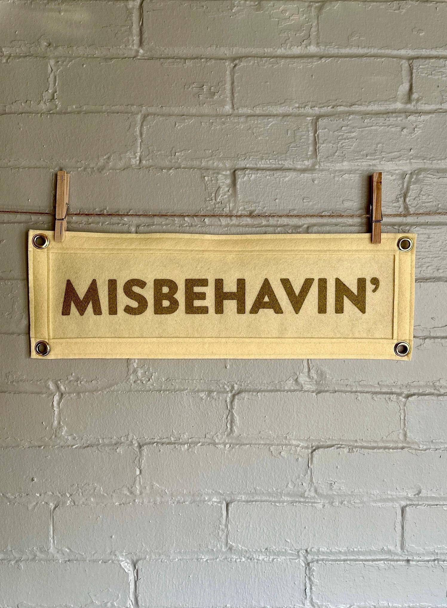 Cream felt banner with cream trim and gold ink lettering that reads "MISBEHAVIN'"