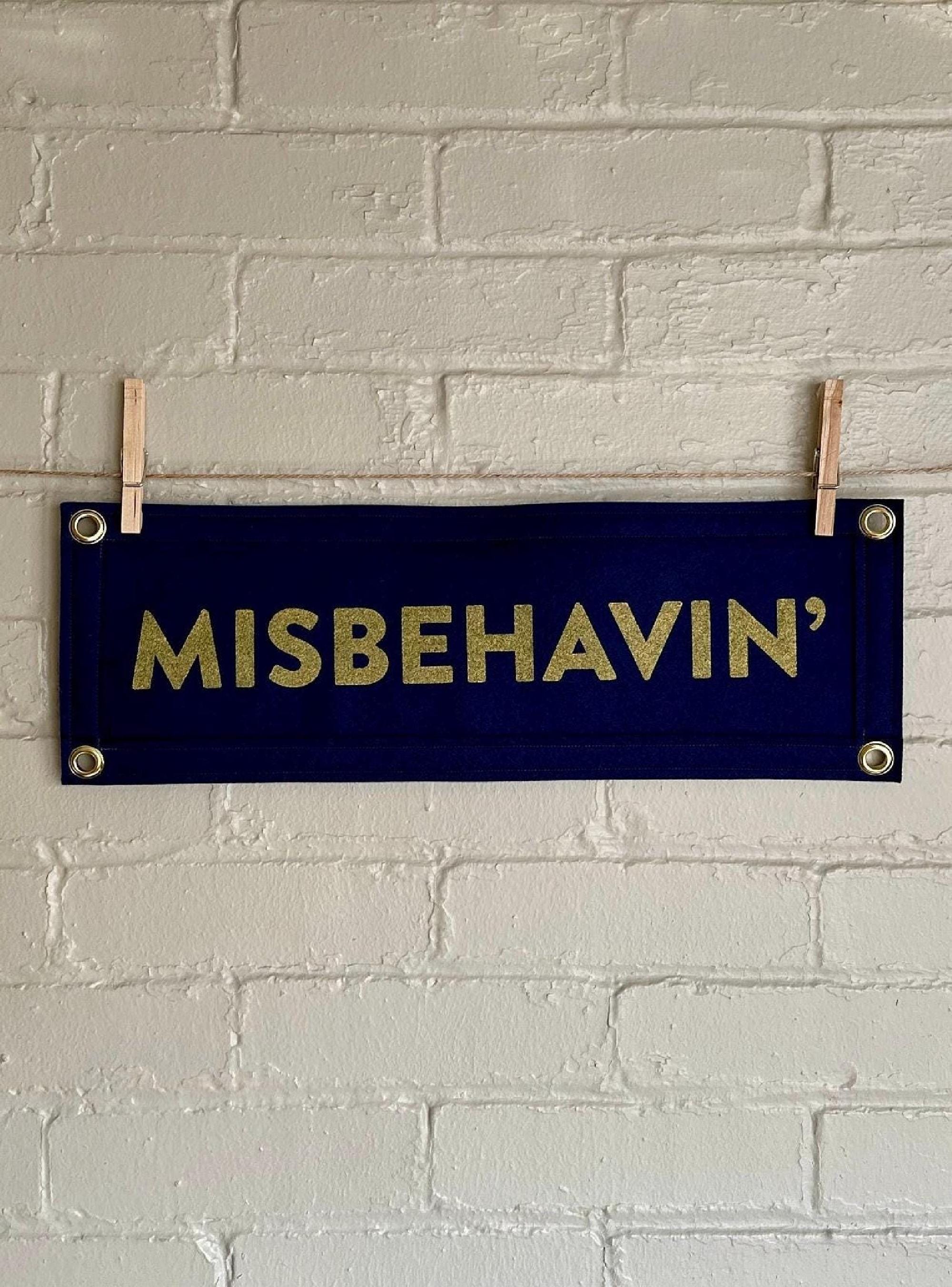 A navy felt banner with navy trim and gold ink lettering that reads "MISBEHAVIN'"