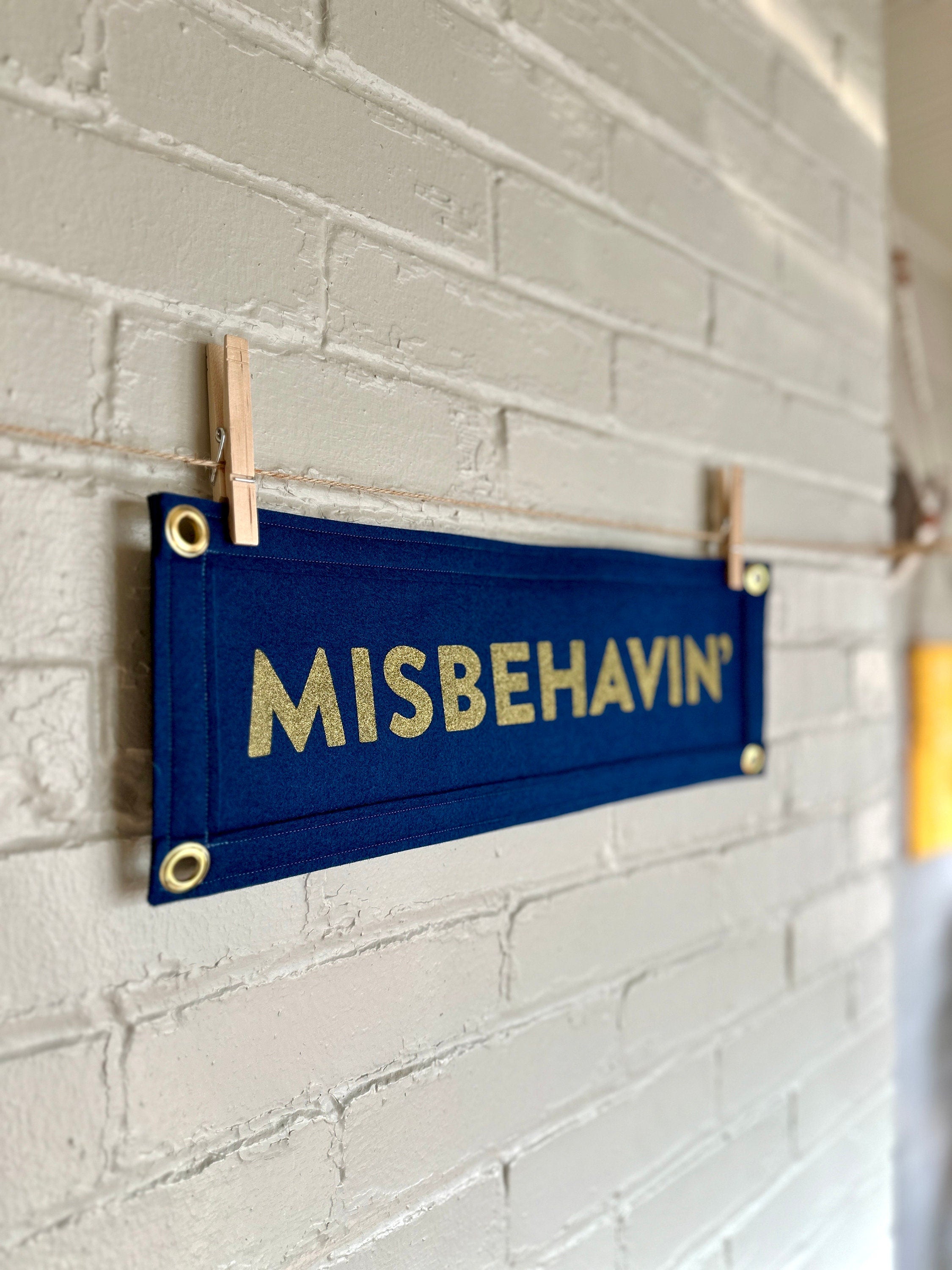 Side view of a navy felt banner with navy trim and gold ink lettering that reads "MISBEHAVIN'"