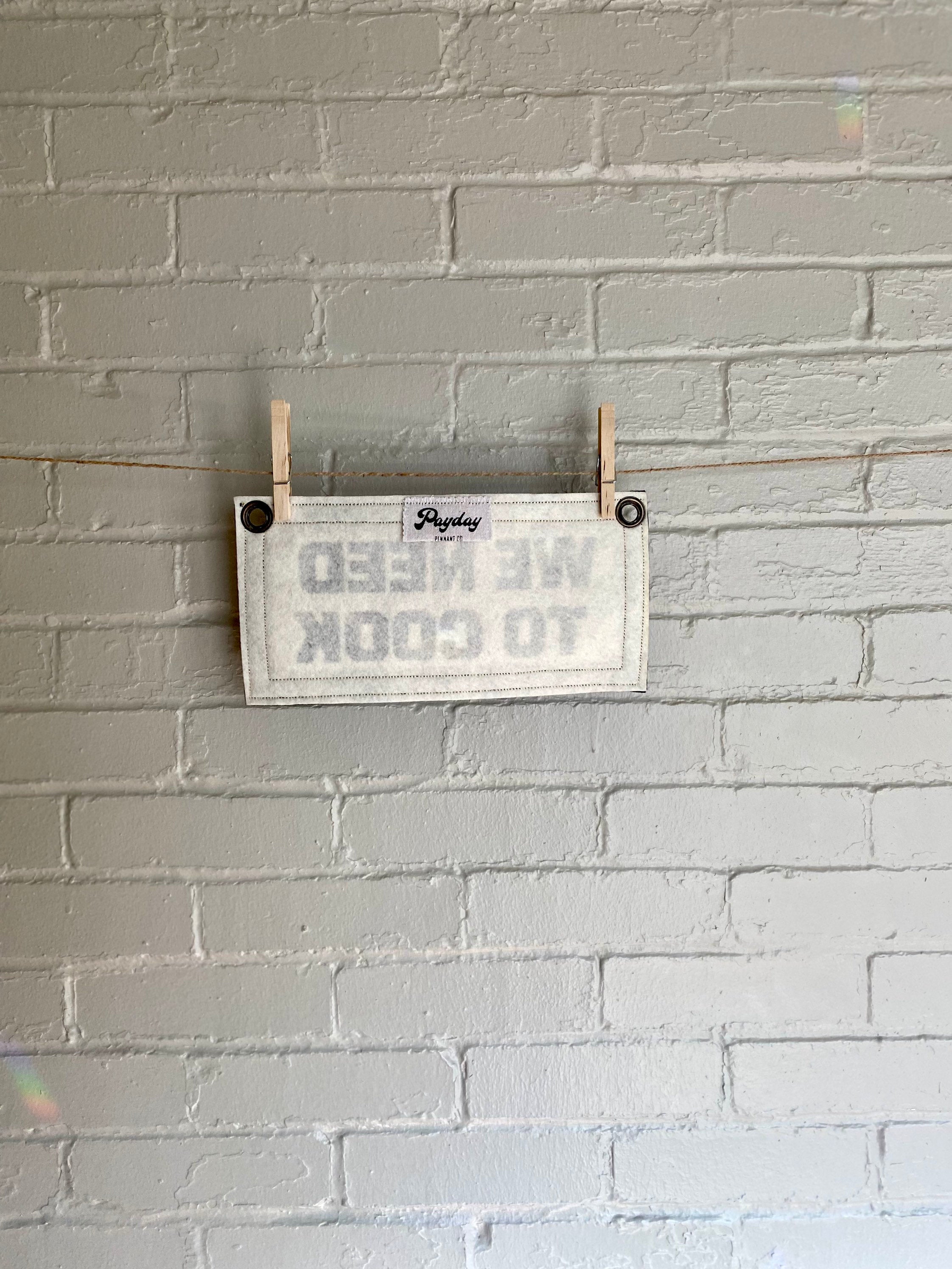 Back of a cream felt banner with black trim and lettering that reads "we need to cook"