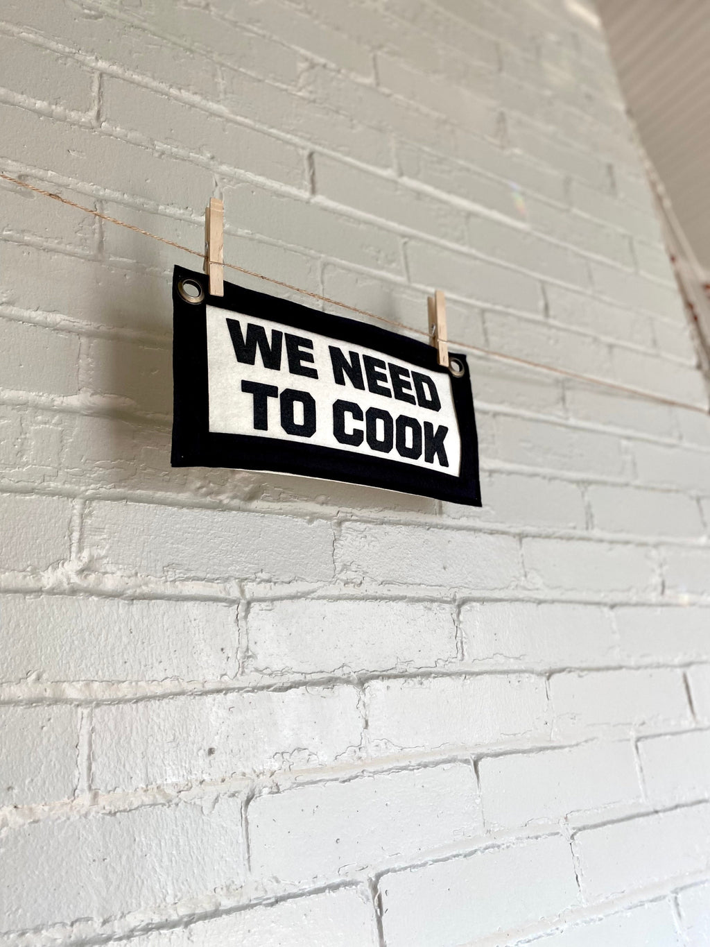 Side view of a cream felt banner with black trim and lettering that reads "we need to cook"