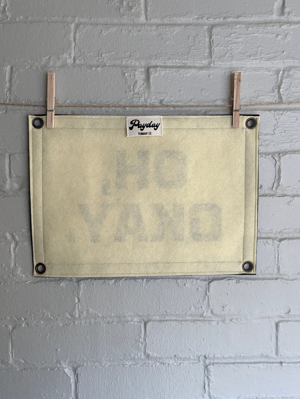 Back of a cream banner with black felt trim and lettering that reads "Oh, Okay."