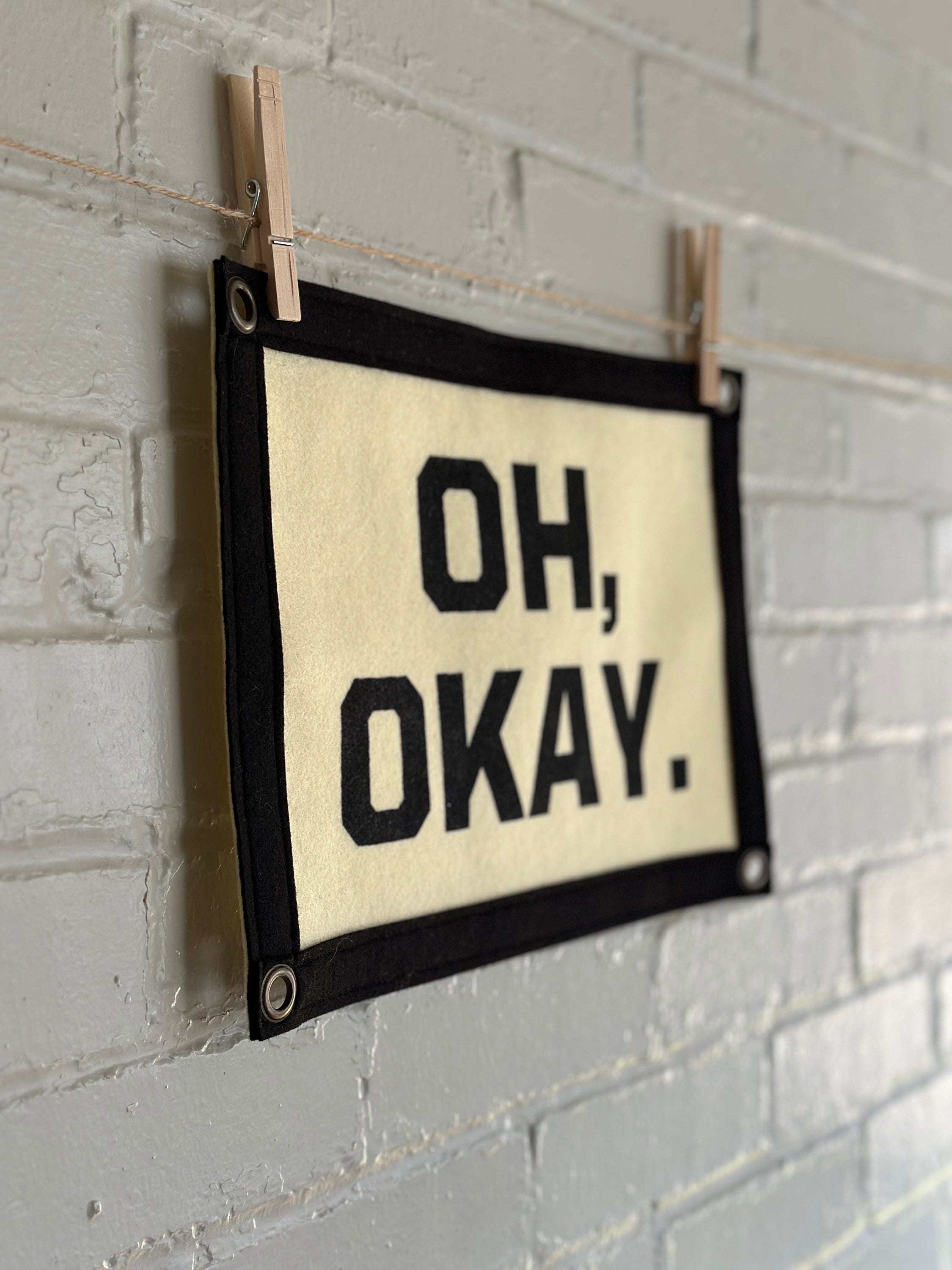 Side view of a cream banner with black felt trim and lettering that reads "Oh, Okay."