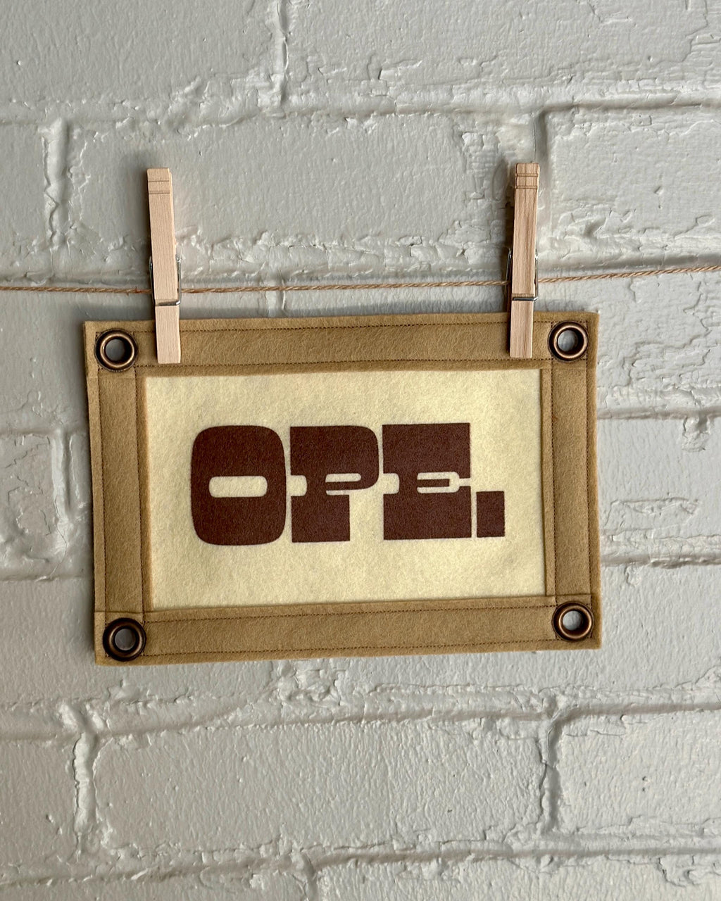 A cream felt banner with light brown trim and brown ink reading "OPE."