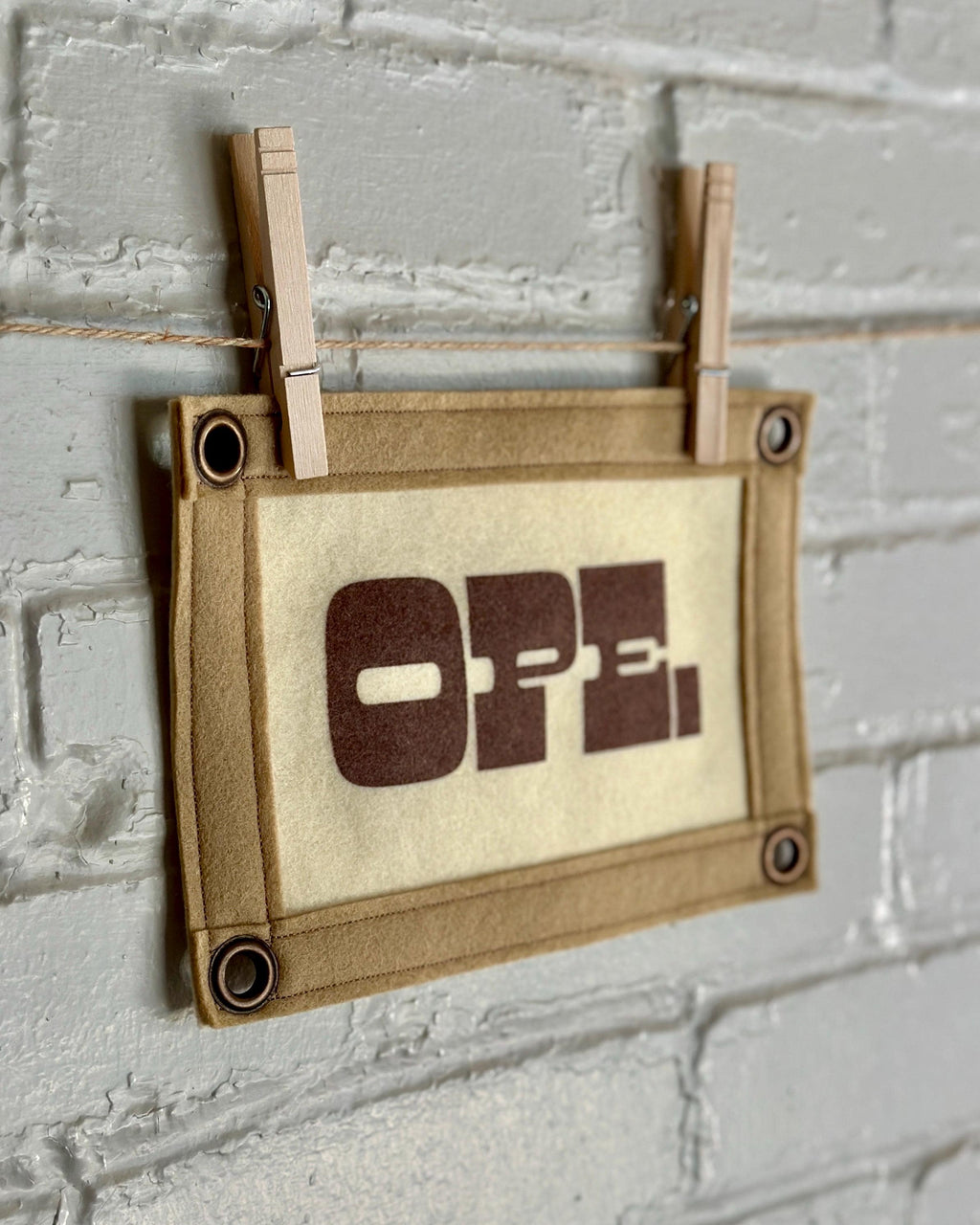 Side view of a cream felt banner with light brown trim and brown ink reading "OPE."