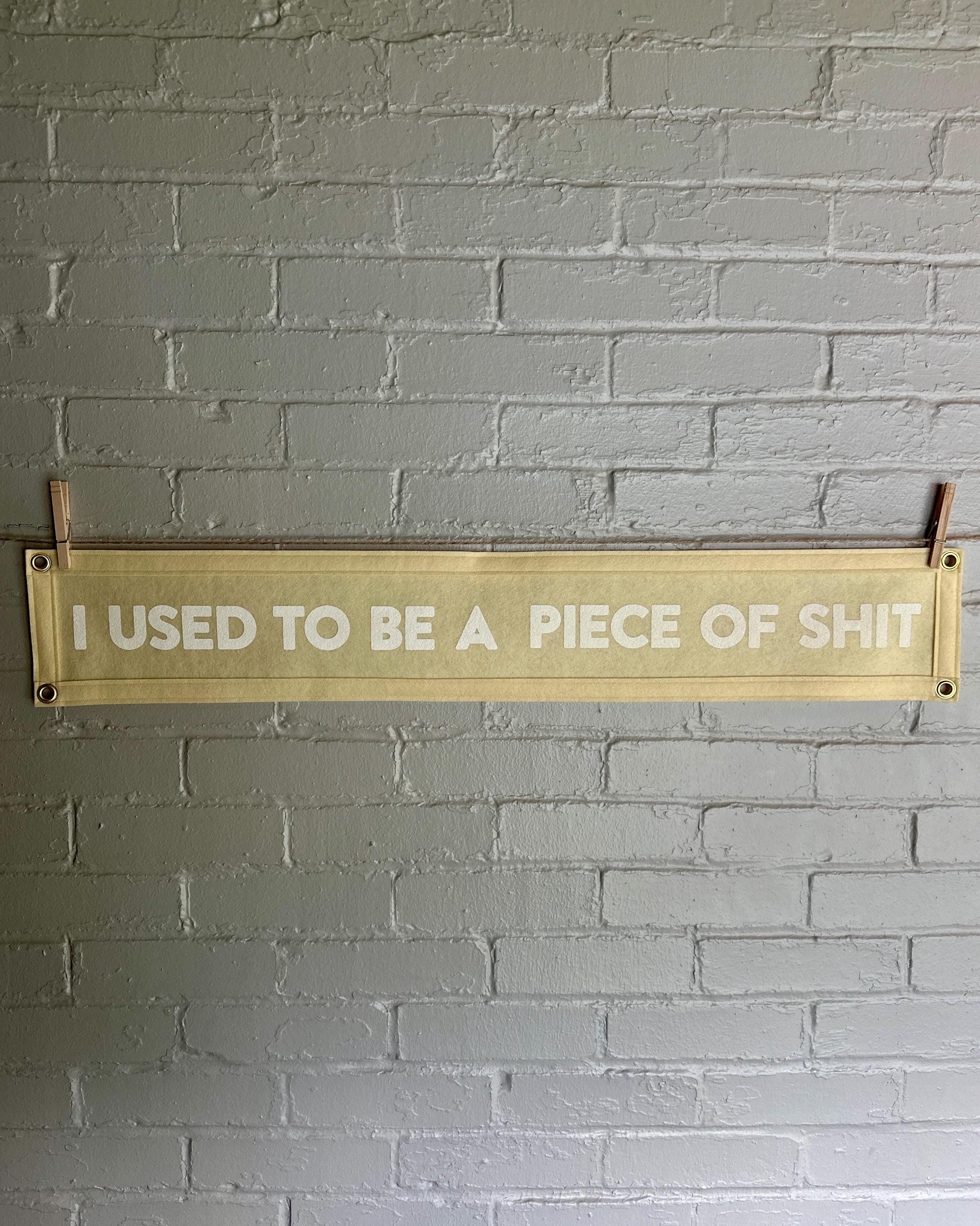 A cream banner with cream trim and white lettering that reads "I used to be a piece of shit"